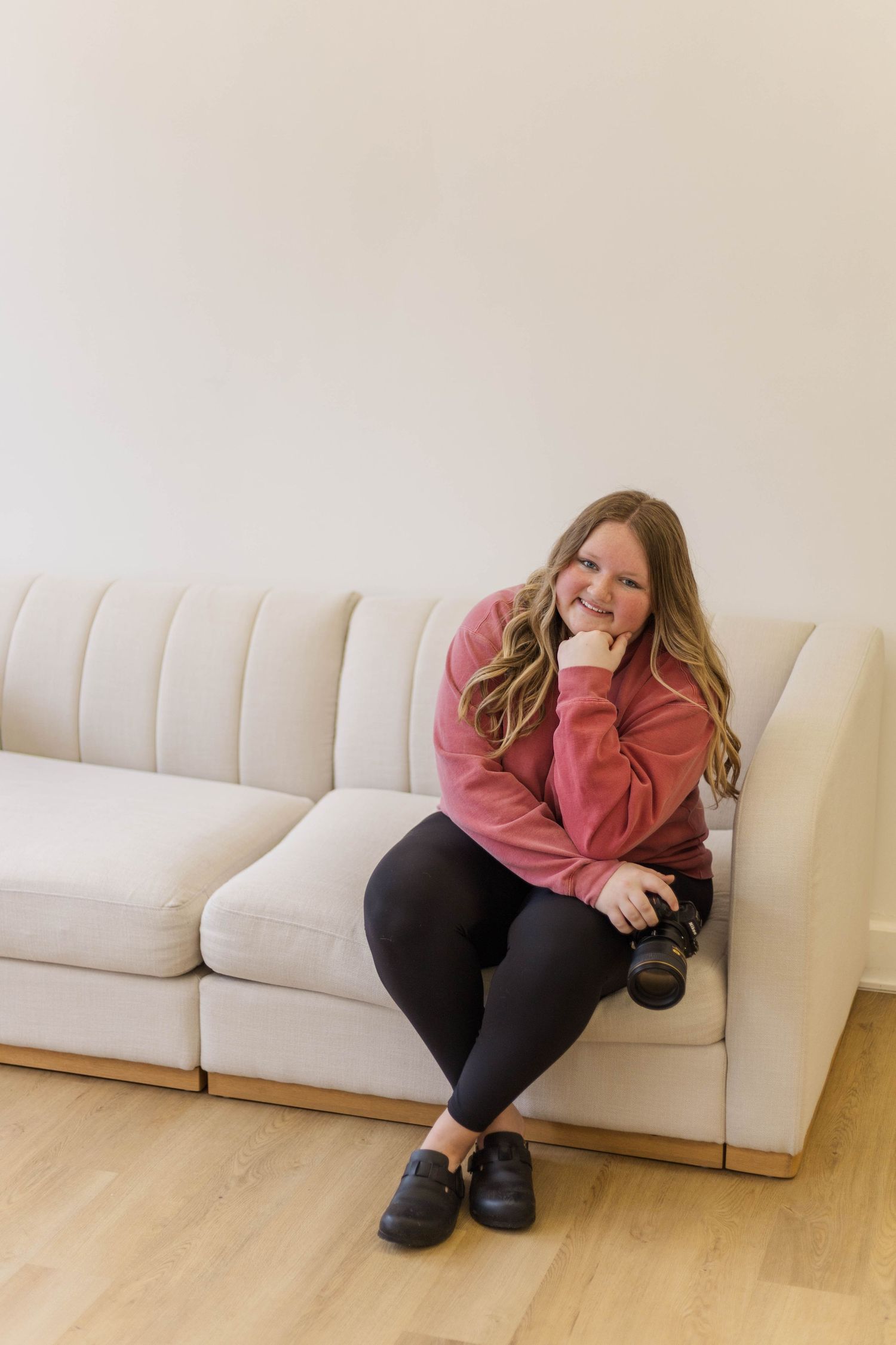Person in pink sweater curled up on white couch in casual pose.