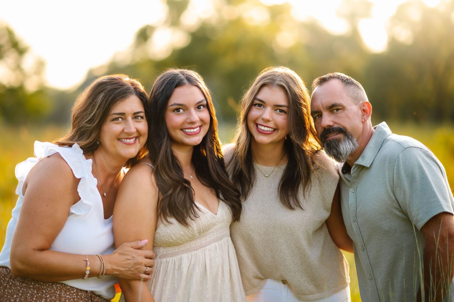 A group poses for portraits in coordinated neutral outfits during sunset in a meadow.