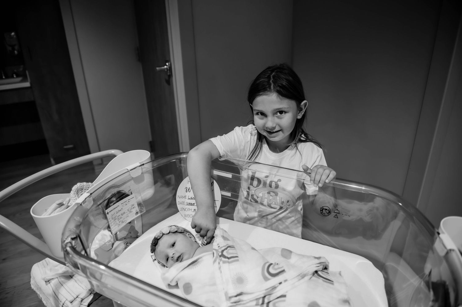 Family members gather close to view a newborn in a hospital bassinet.