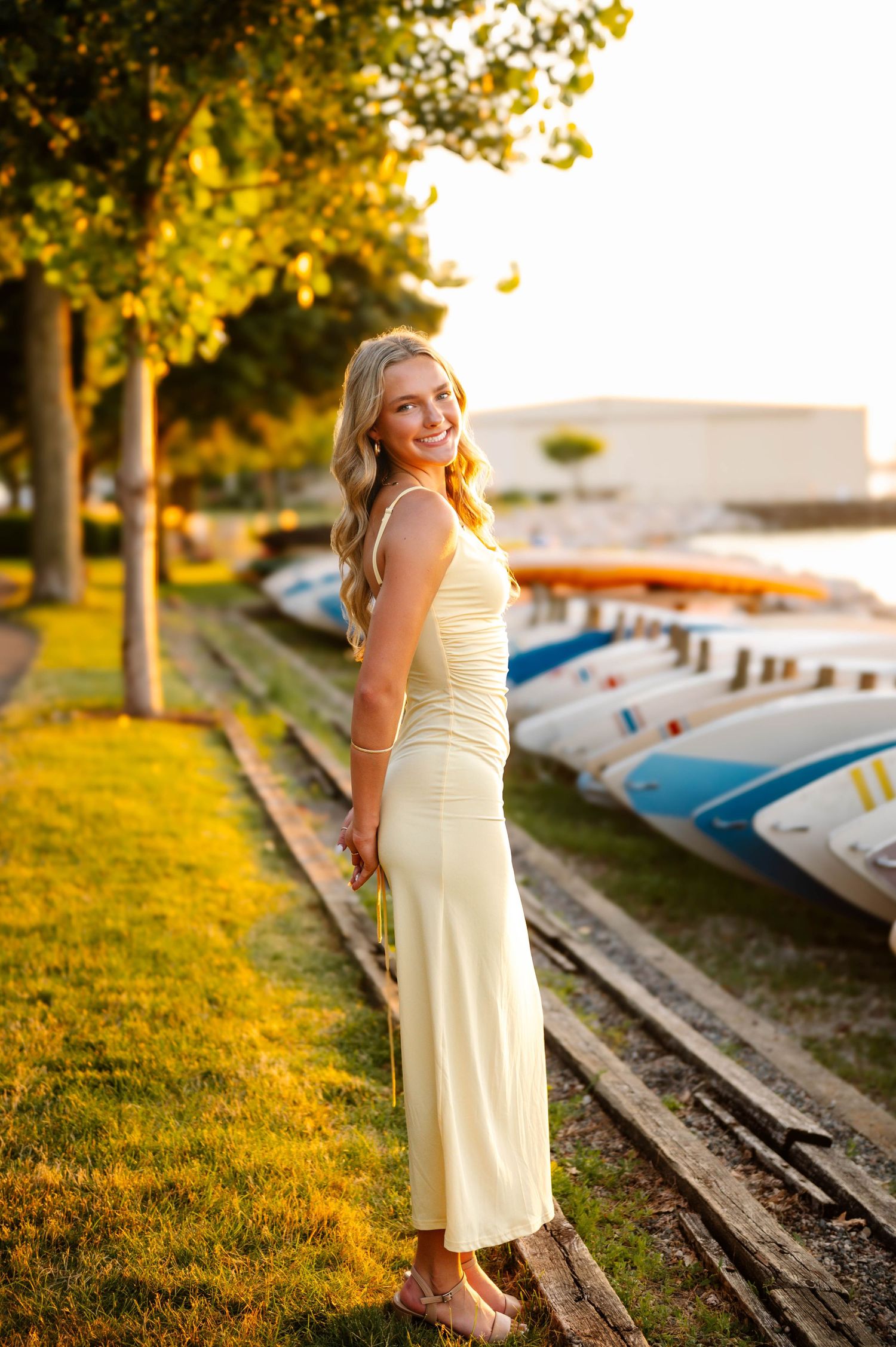 Summer evening photoshoot by a lakeside with boats in background during golden hour.
