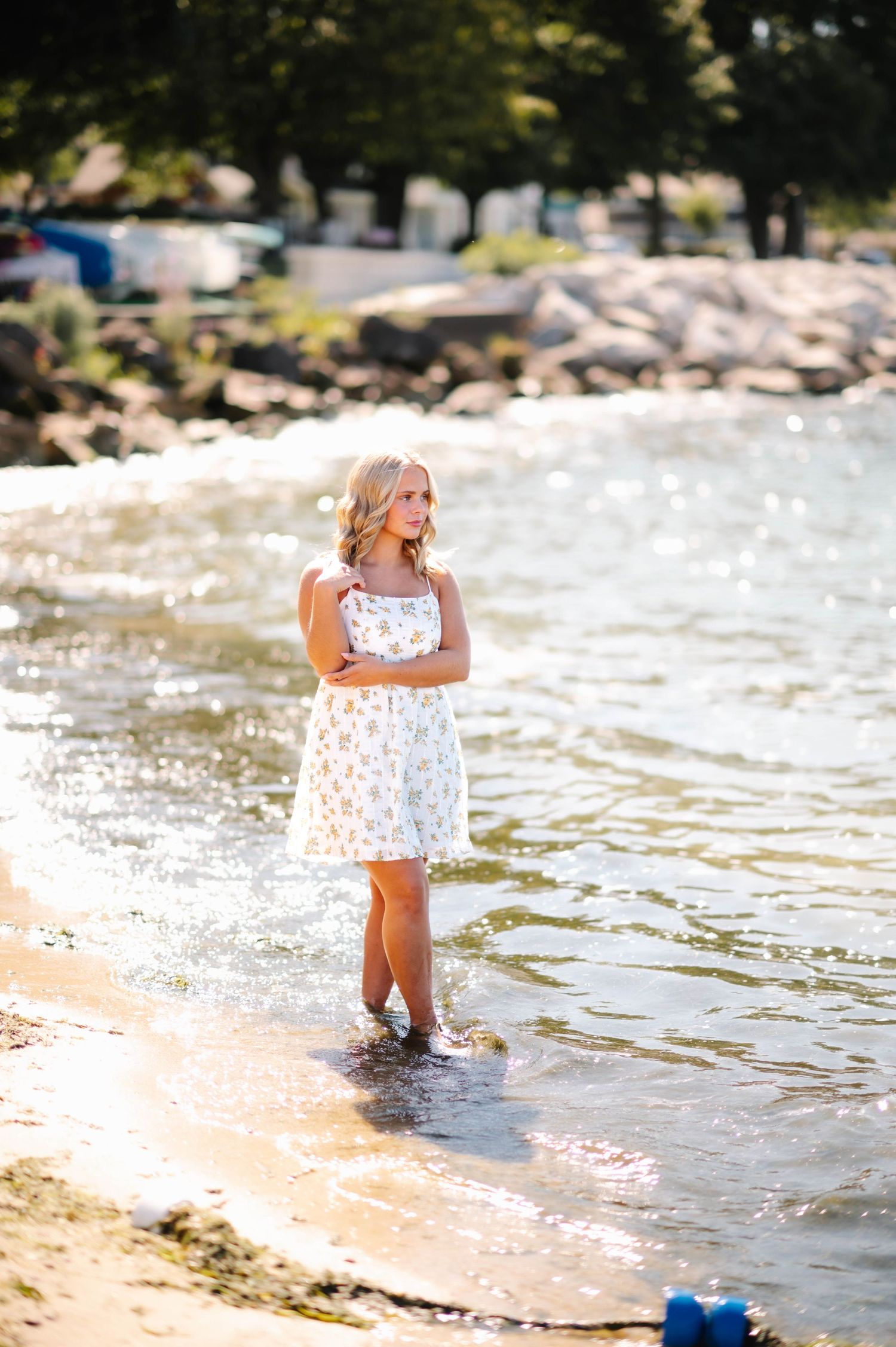 Woman in white dress splashing and playing in shallow ocean waves at sunset on a rocky beach.