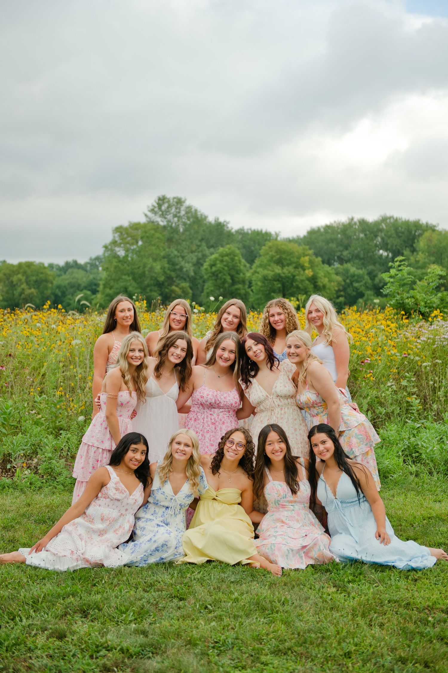 A group of teenage girls in floral dresses pose together in a wildflower field for a senior portrait session.