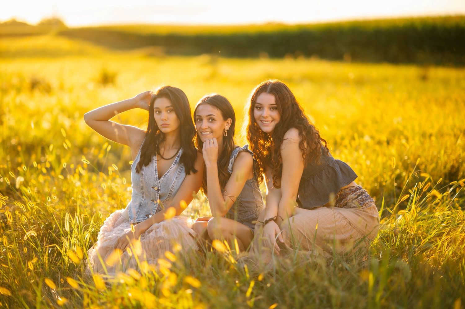 Three friends pose together in a sunlit wildflower field at sunset.