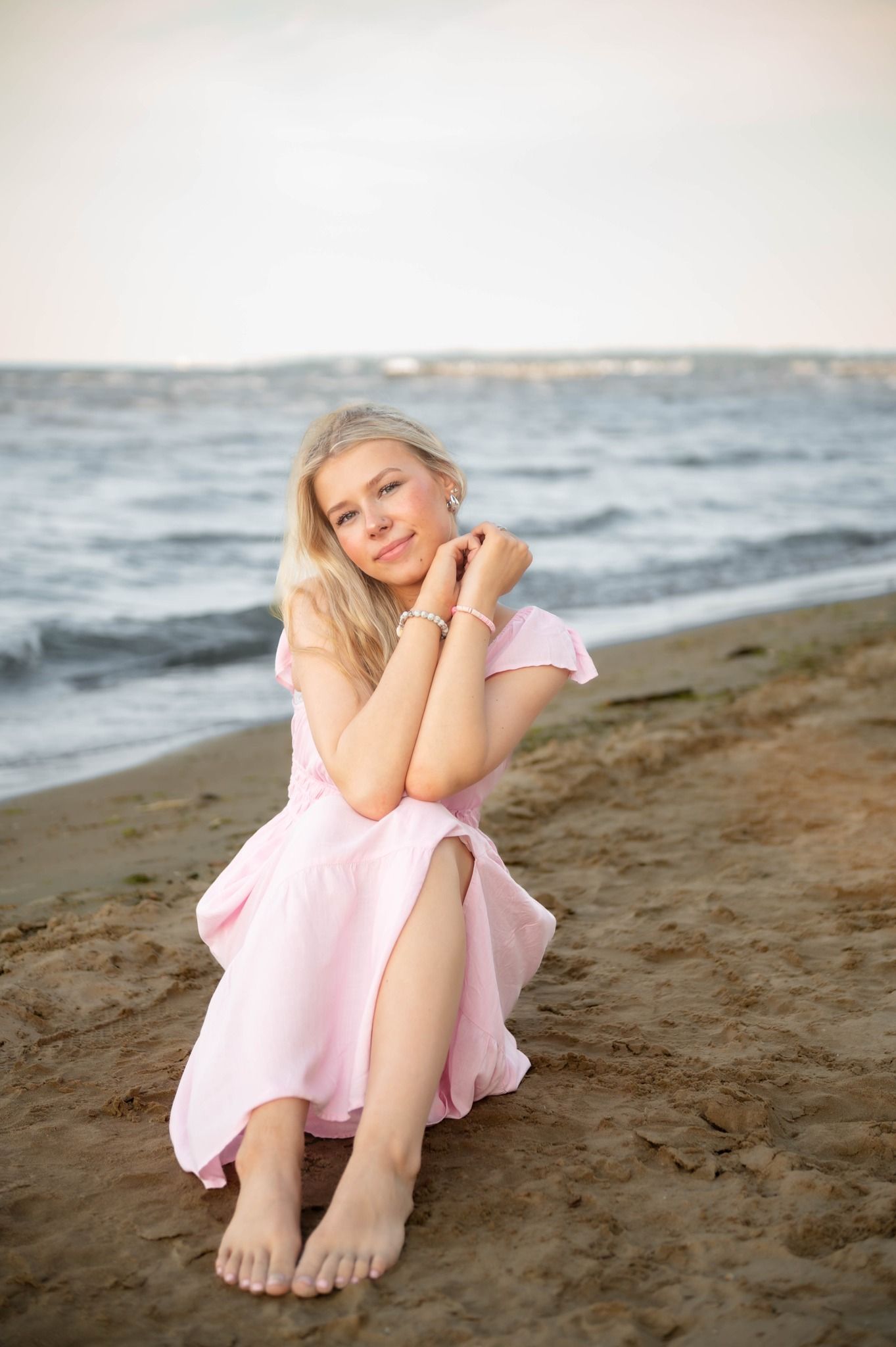 Someone wearing a pink dress relaxes on the sandy beach near the ocean waves.