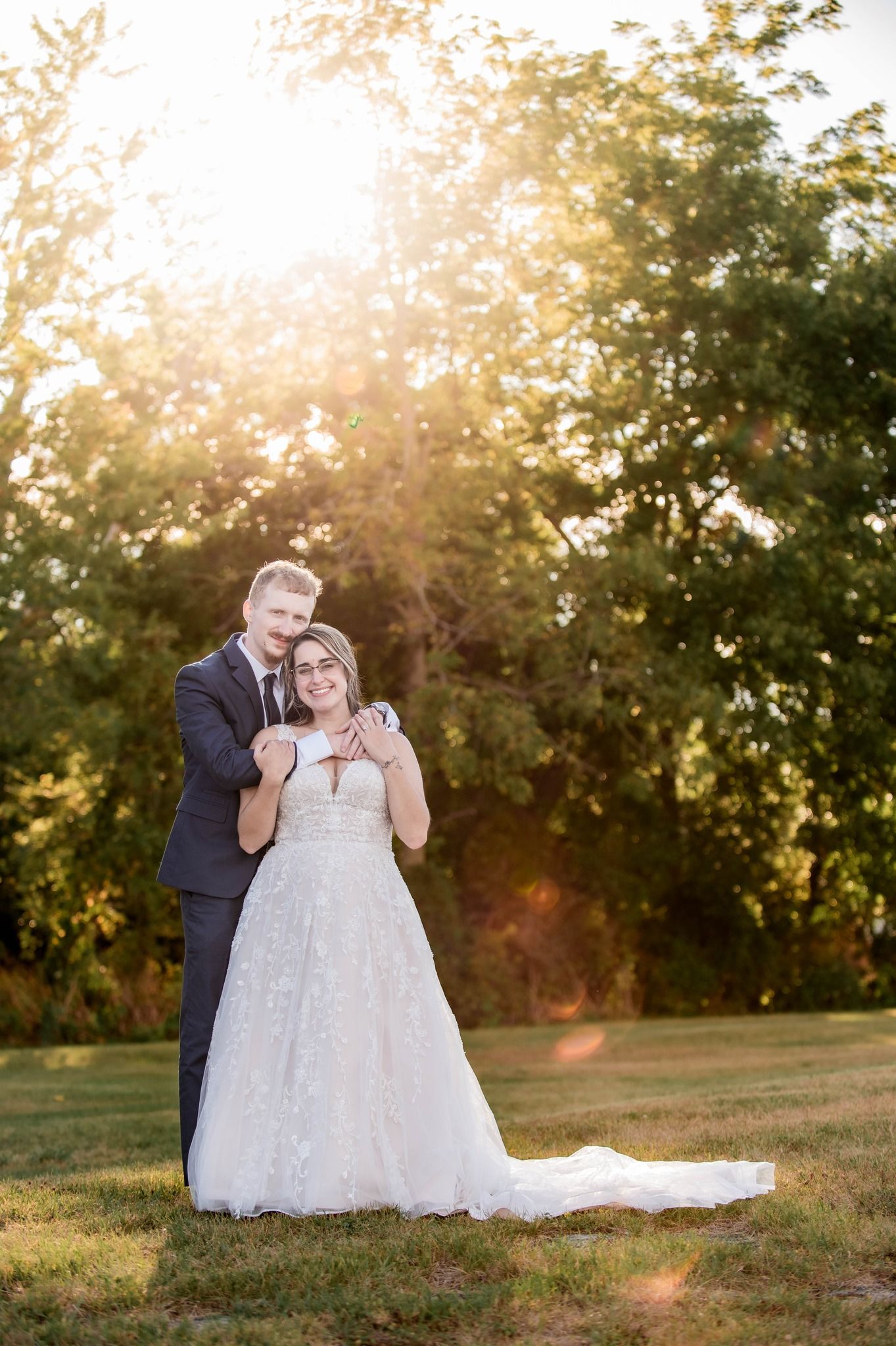 Wedding couple shares intimate moment in a sunlit outdoor setting with trees in background.