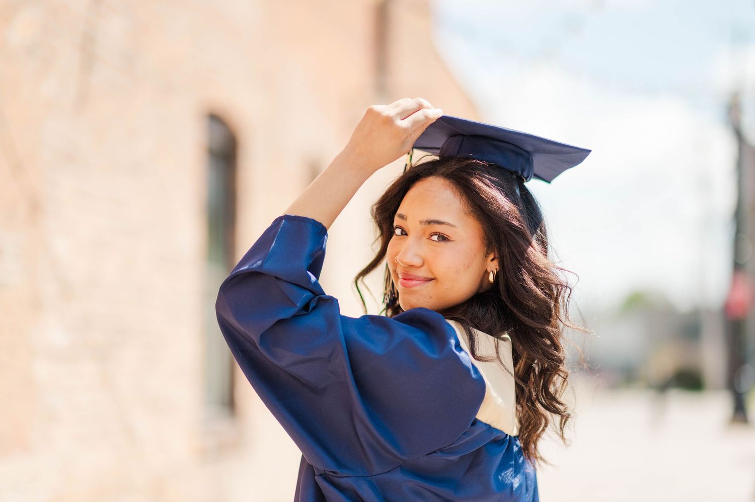 Smiling female graduate in blue cap and gown posing outdoors in natural light.