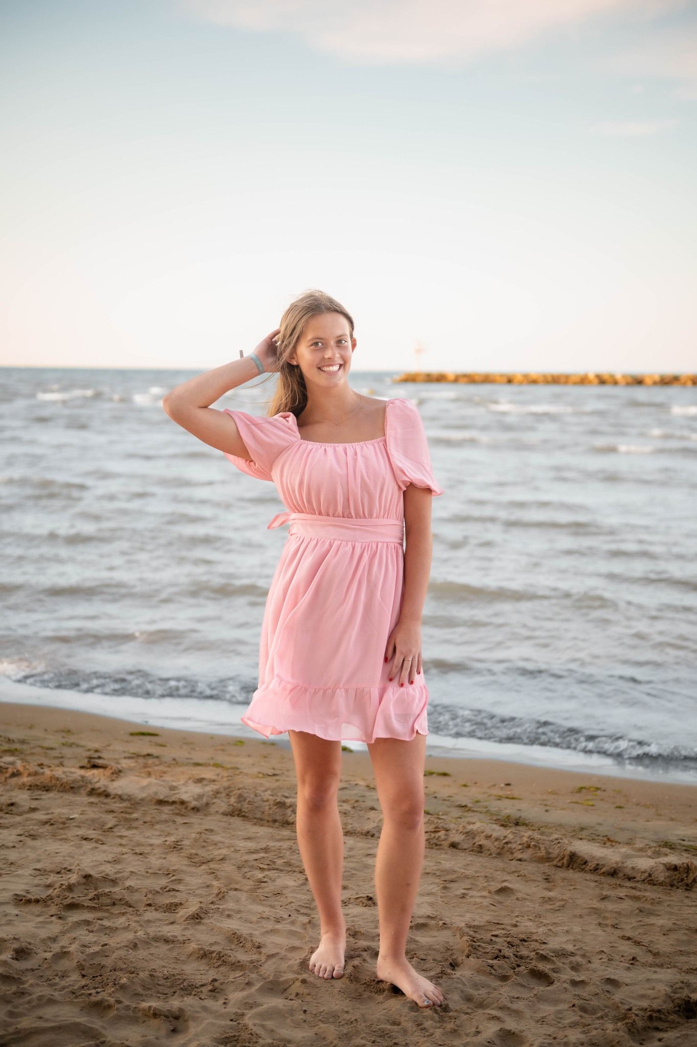 Playful poses on beach in flowing pink dress against ocean backdrop.