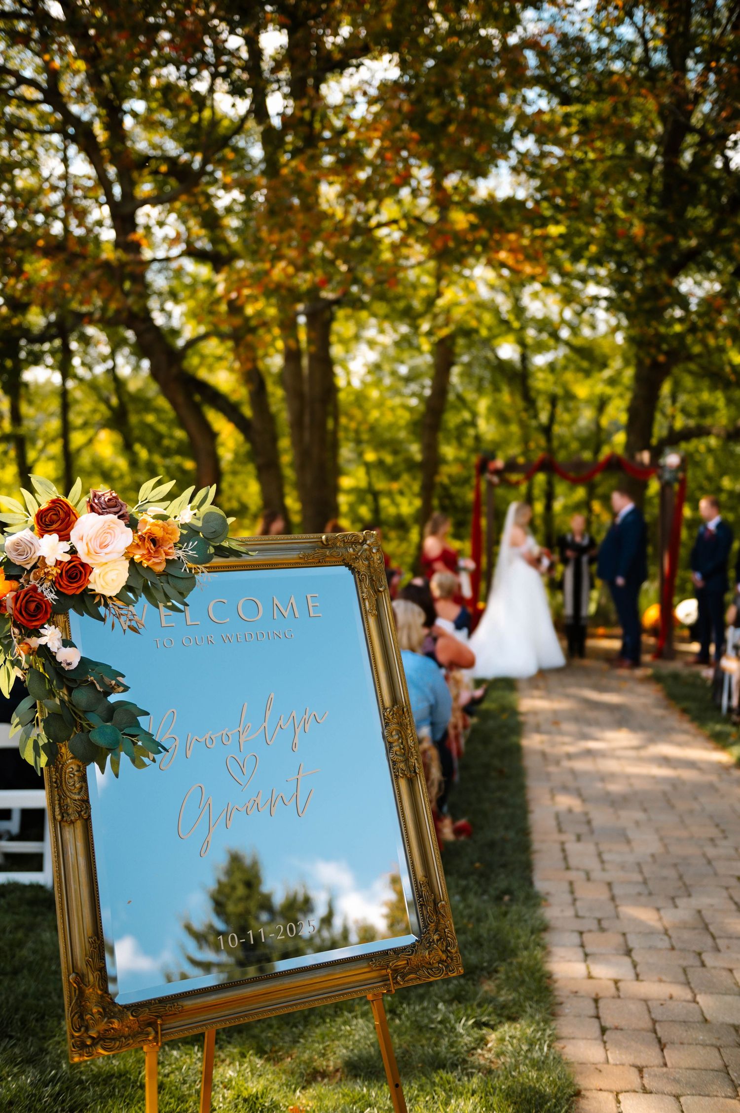 Welcome signs with floral decorations line stone pathway at outdoor wedding venue.
