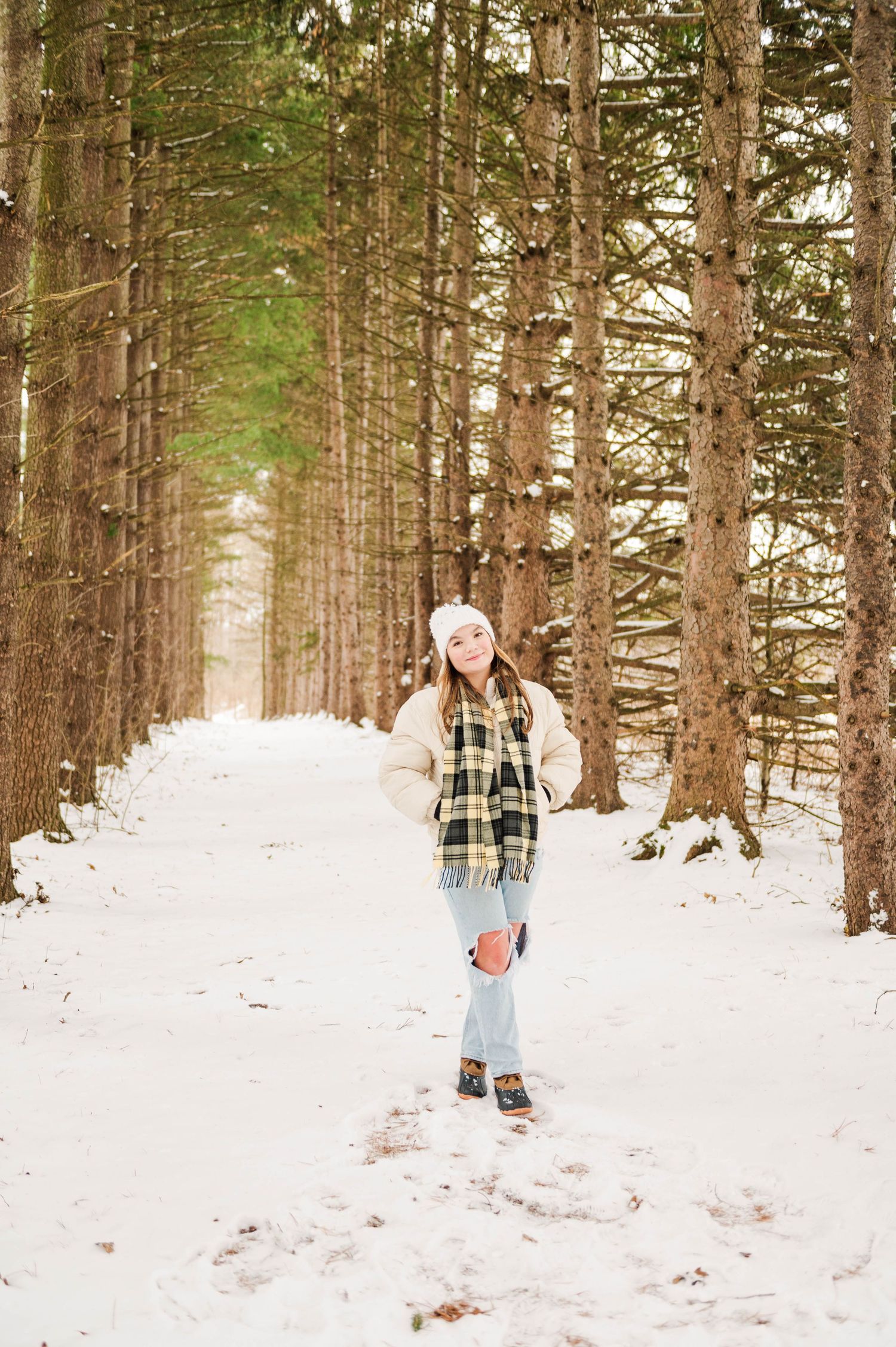 Person walking through snow-covered pine forest wearing plaid and denim.