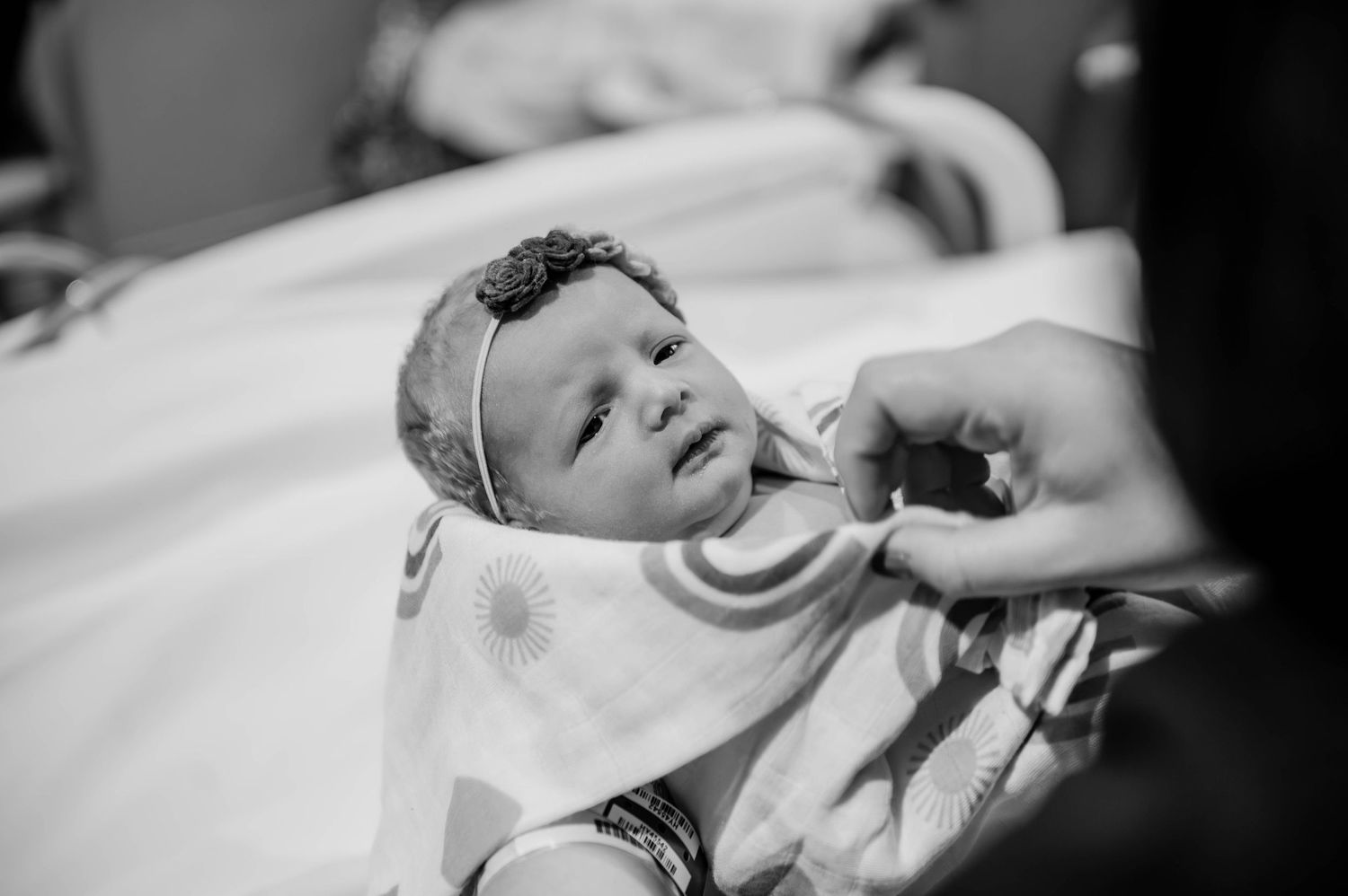 Close-up black and white portrait of a newborn baby with a decorative headband in the hospital.