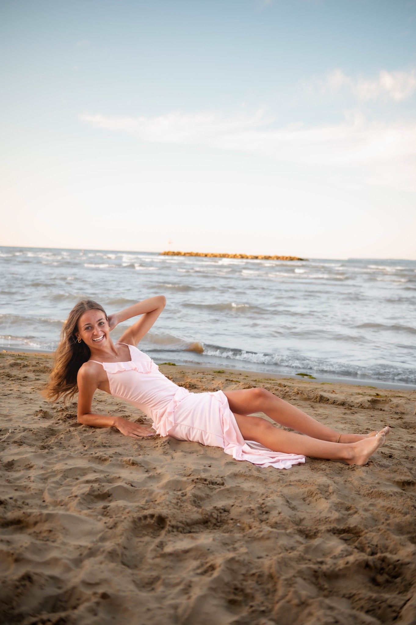 Someone in a pink dress reclines gracefully on the sandy beach at sunset.