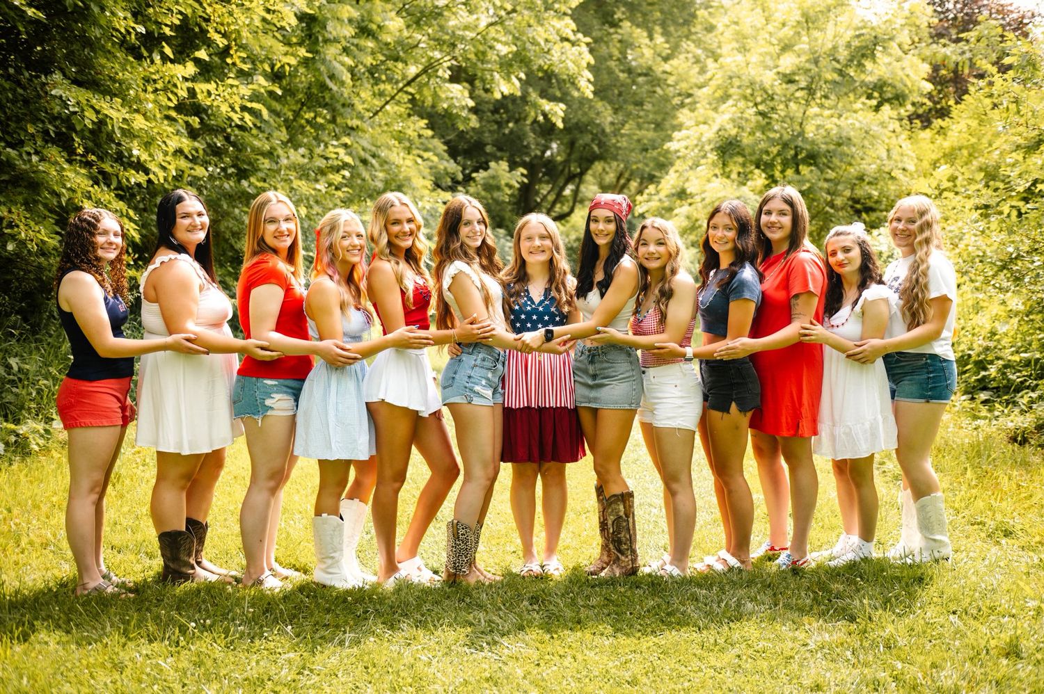 Large group in red white and blue outfits pose together holding American flag outdoors.