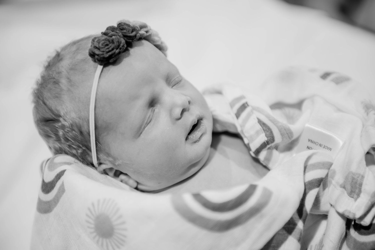Serene black and white portrait of a sleeping newborn wearing a delicate headband.