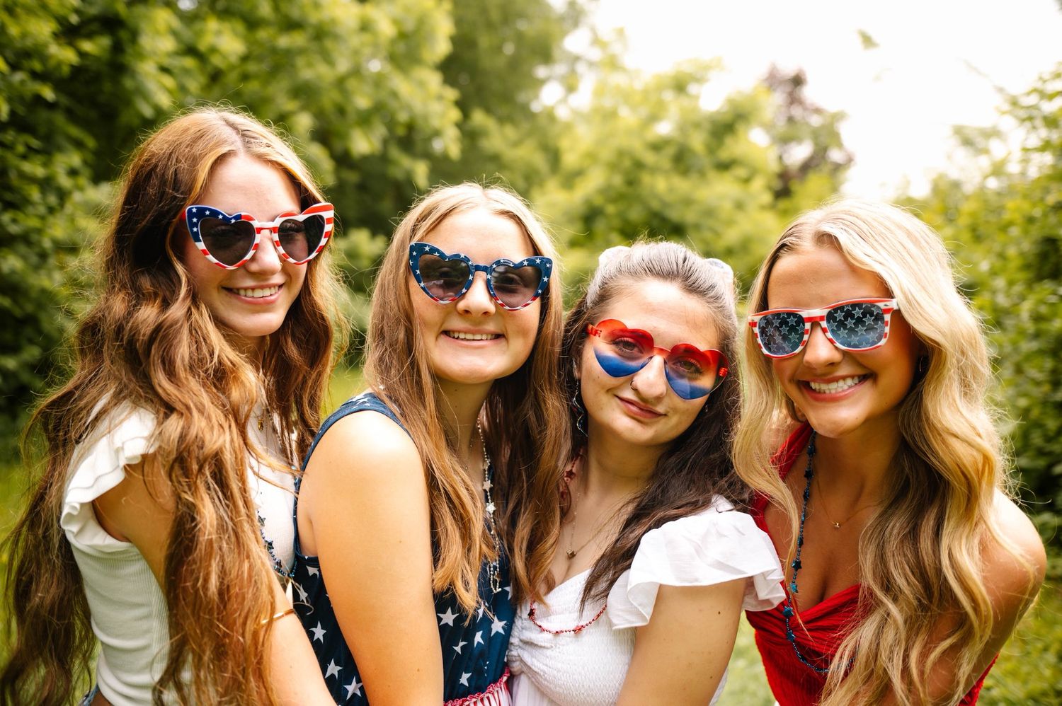 Four friends wearing festive sunglasses pose together for summer photo.