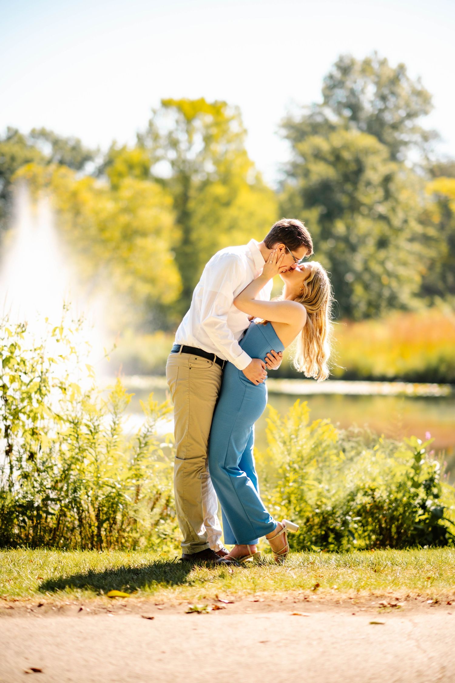 A couple sharing an intimate moment by a lake with golden sunlight and trees in the background.