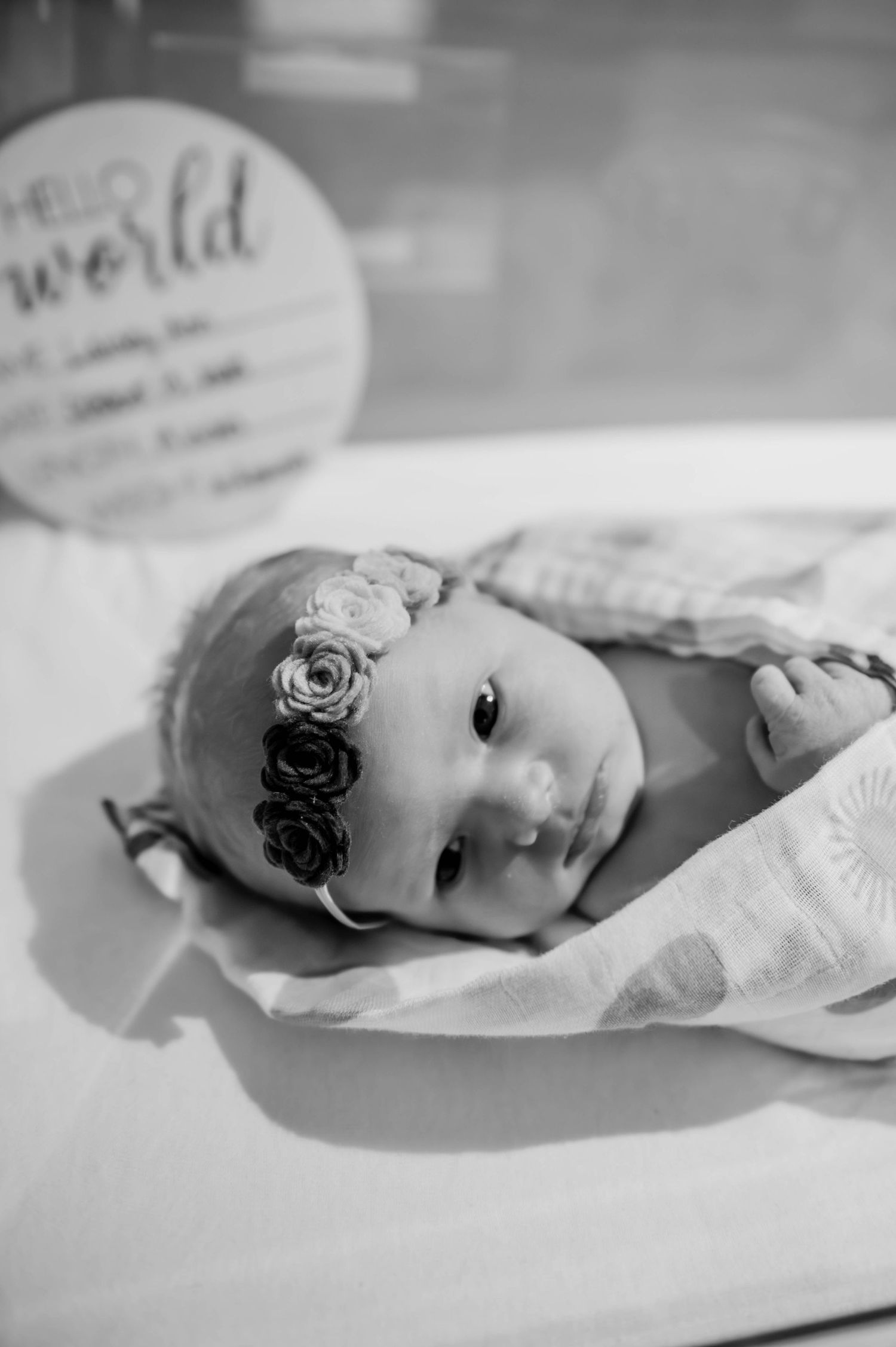Side view of a newborn baby with floral headband in hospital bassinet.