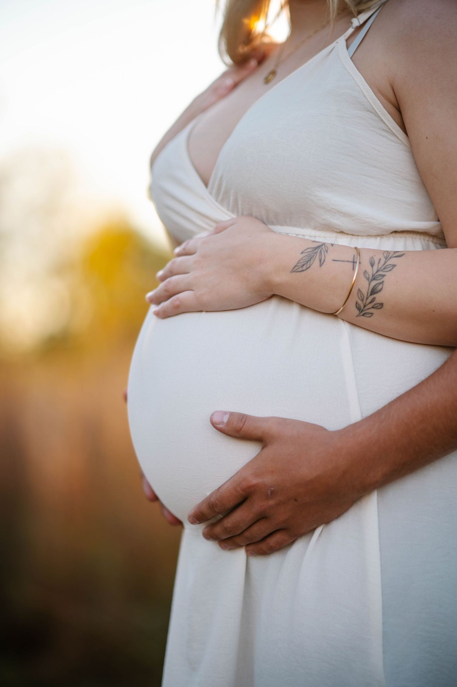 Detailed shots of pregnant belly with delicate hands and floral tattoo.