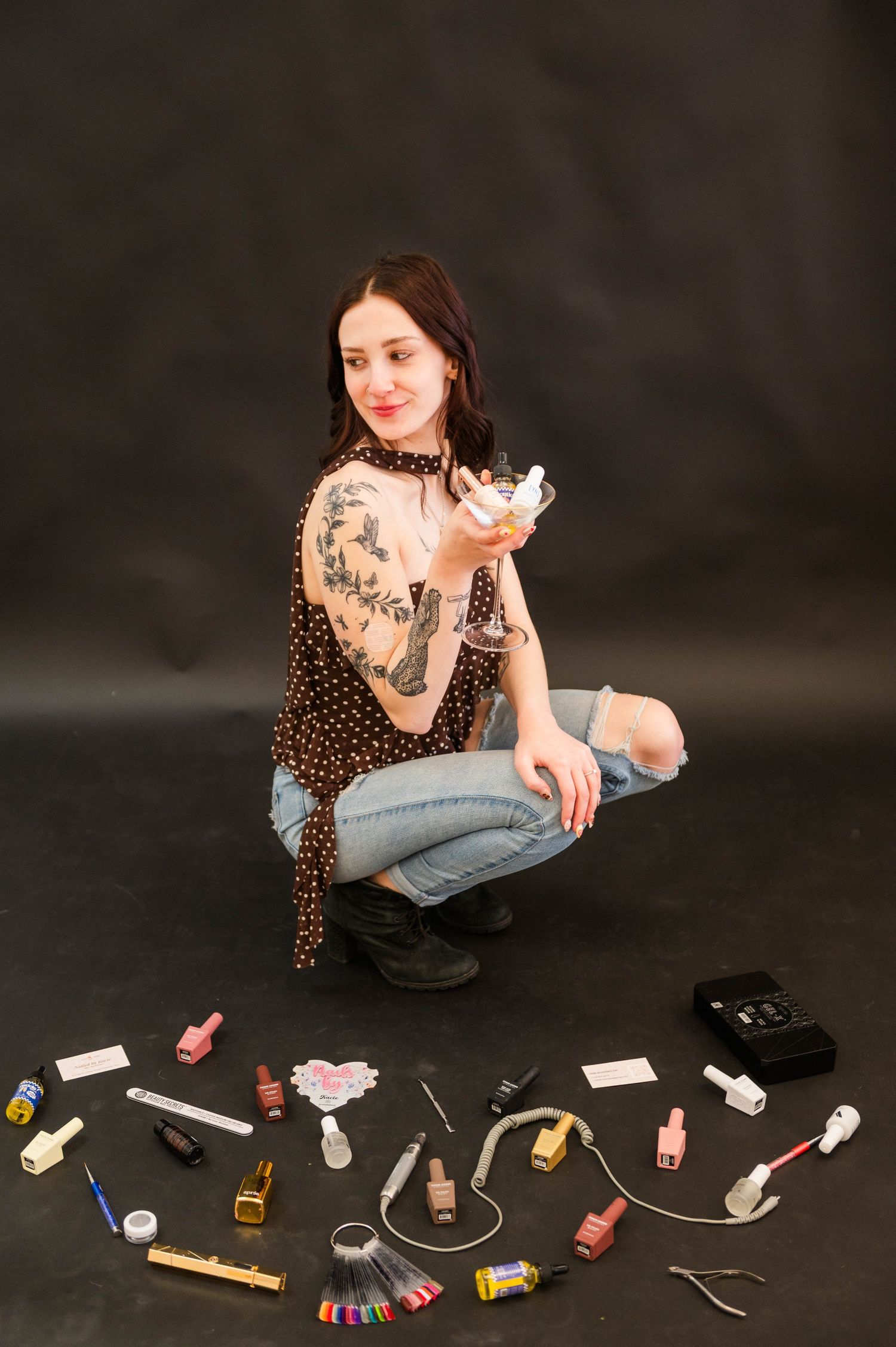 A polka dot top and jeans outfit shown with nail polish and beauty supplies arranged on dark background.