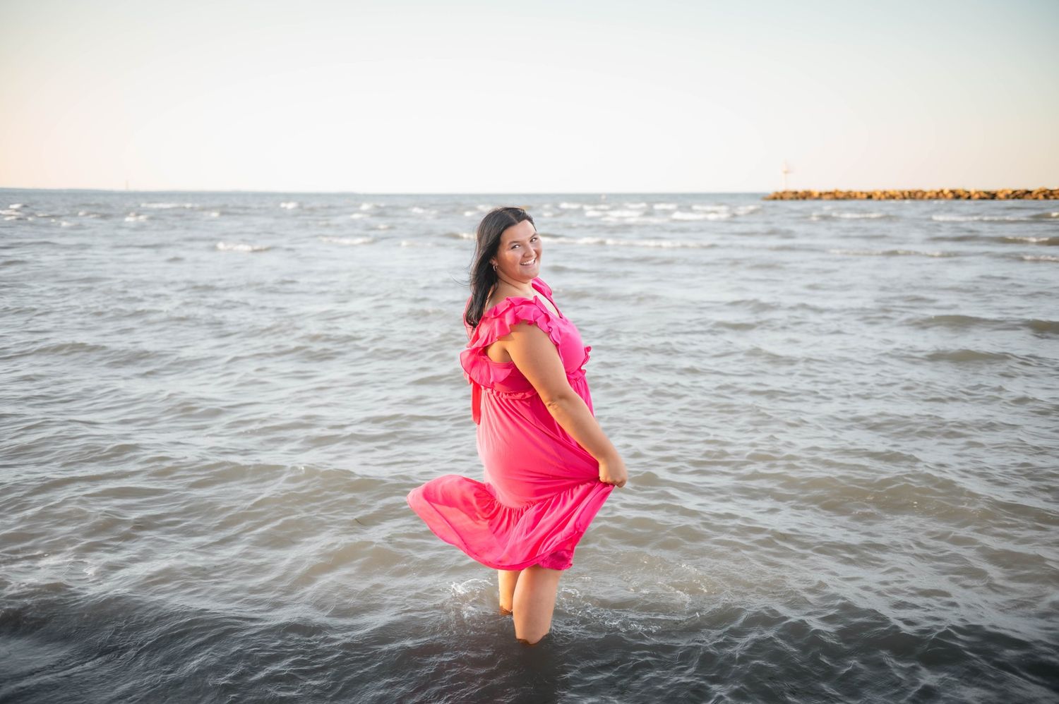 Person in flowing pink dress jumping and splashing in ocean water.
