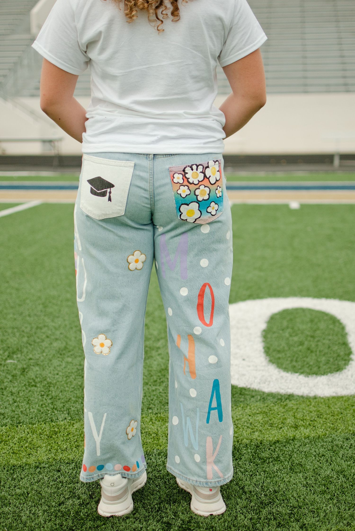 Back view of decorated senior graduation jeans featuring floral patches, cap design, and painted letters.