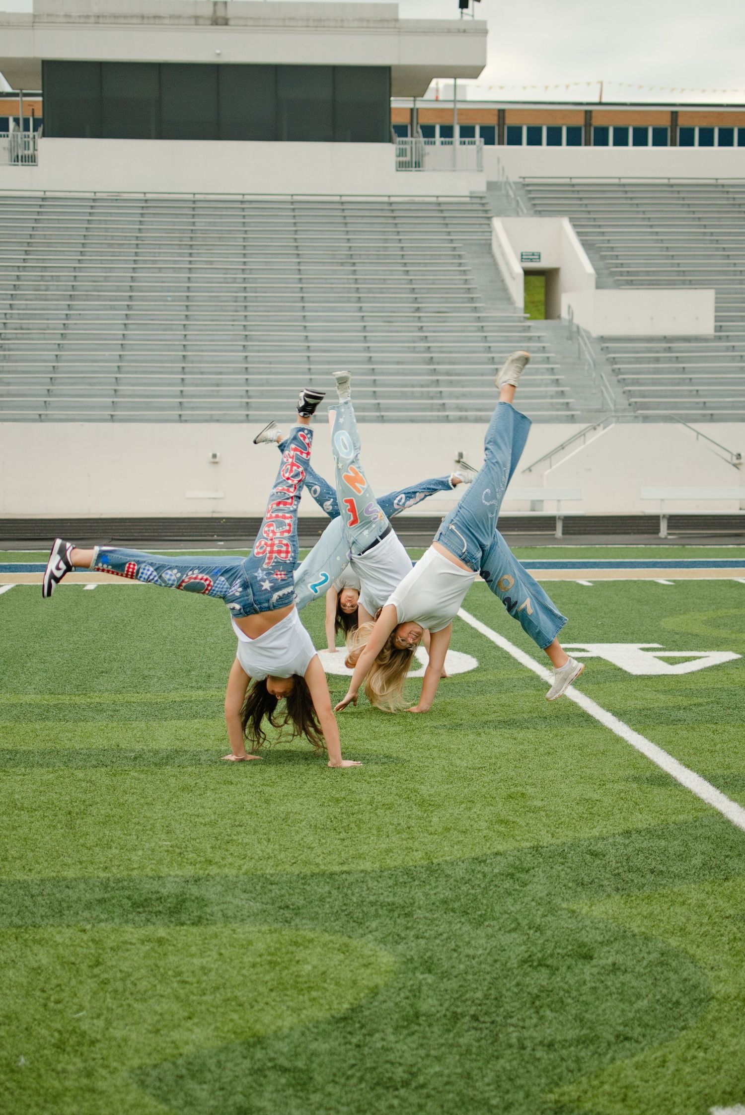 Three girls doing cartwheels on a football field wearing painted denim jeans.