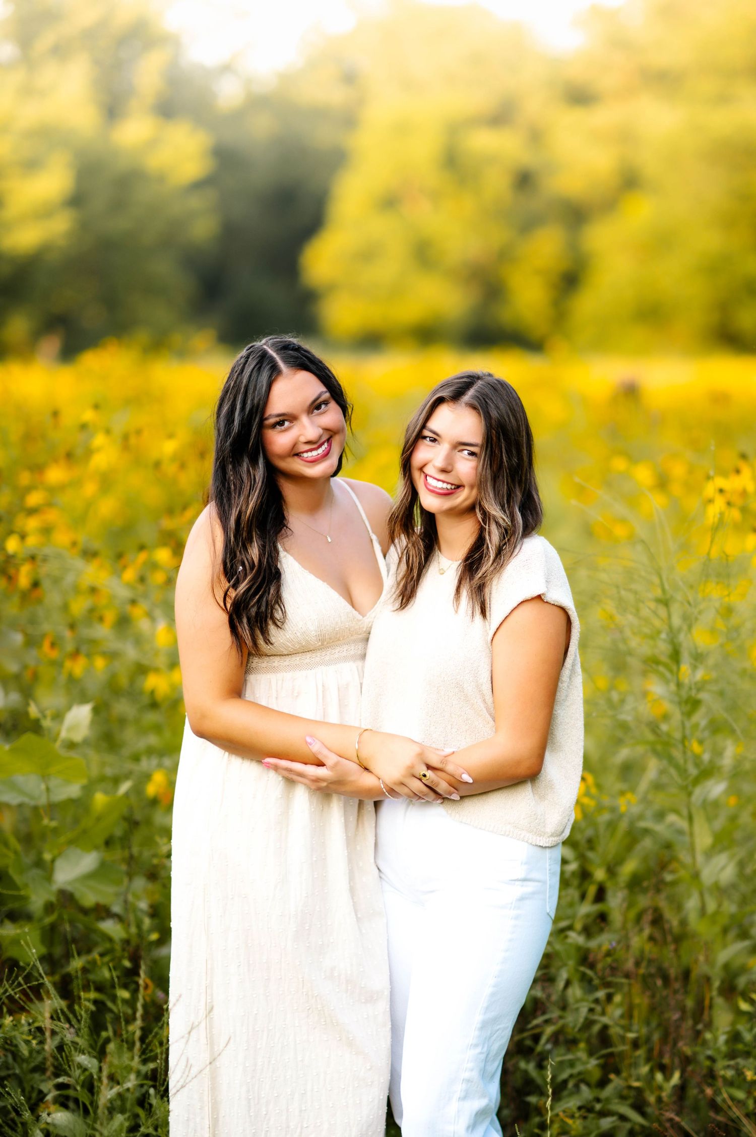 Two people share an embrace while standing in a field of yellow flowers at golden hour.