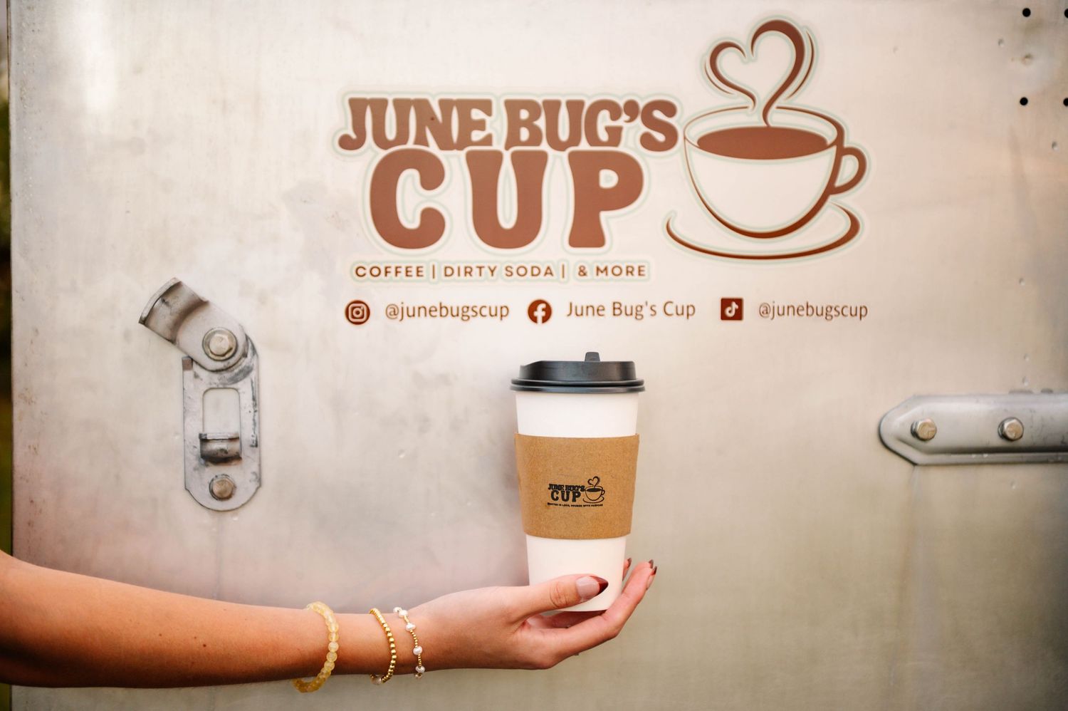 Coffee shop storefront with white exterior and logo displaying 'June Bug's Cup' and a heart design.