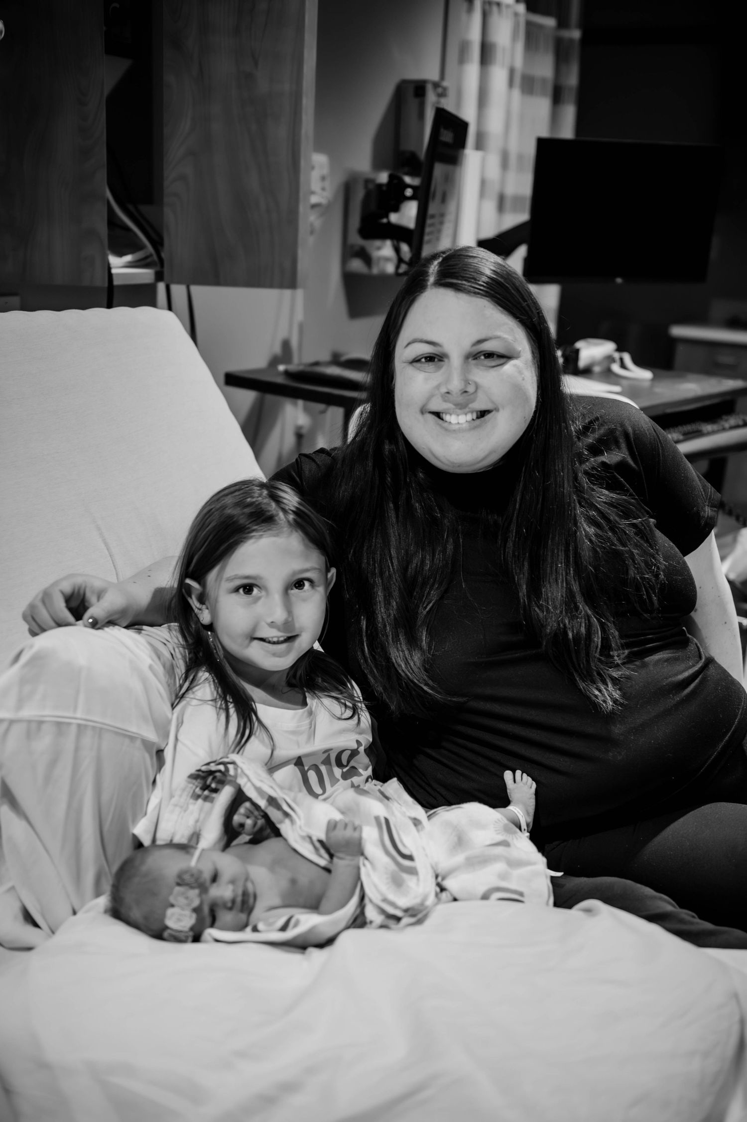 Black and white photograph showing tender family moments on a bed.