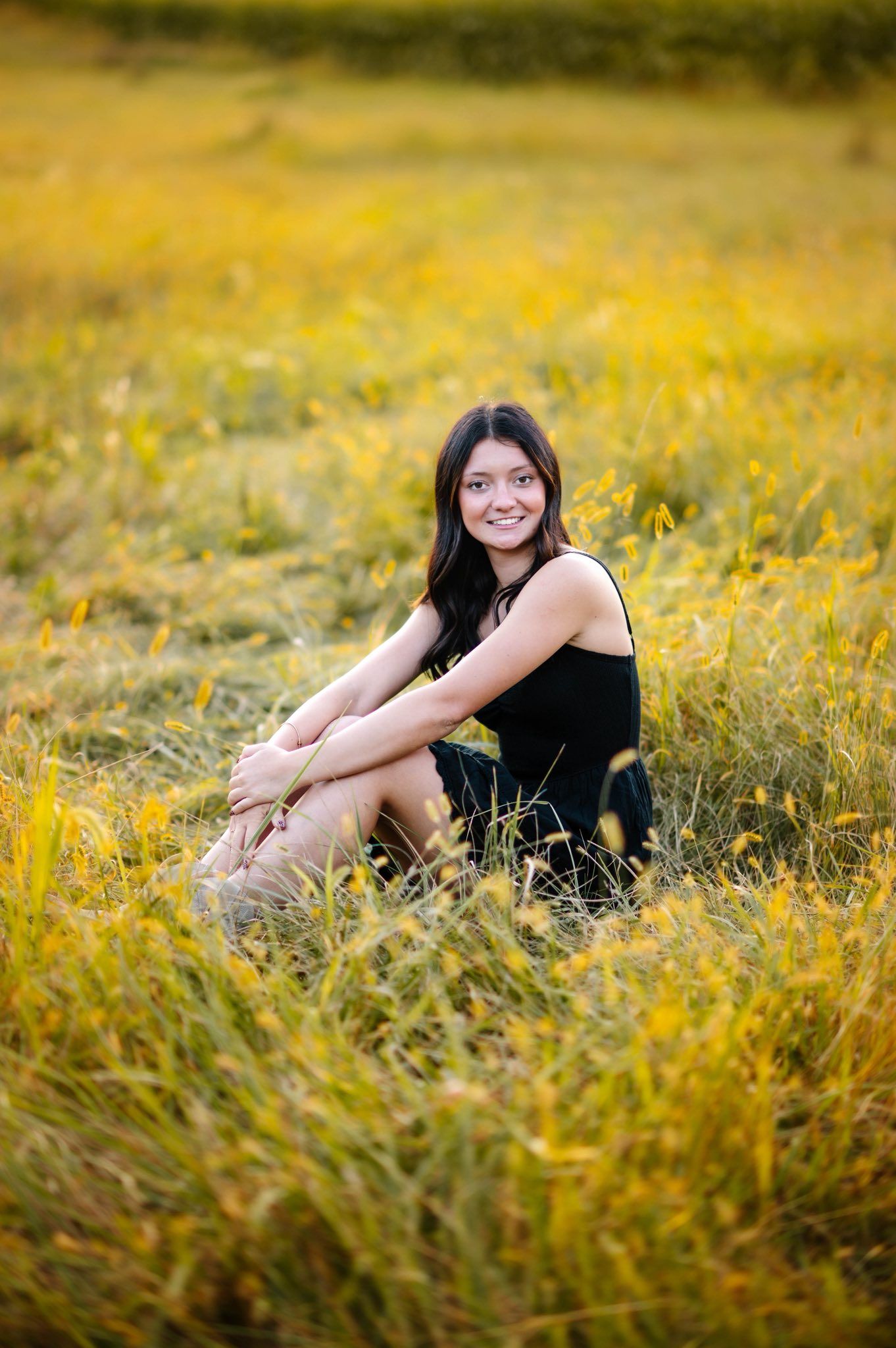 Person in black outfit sitting in tall grass during golden hour photography session.