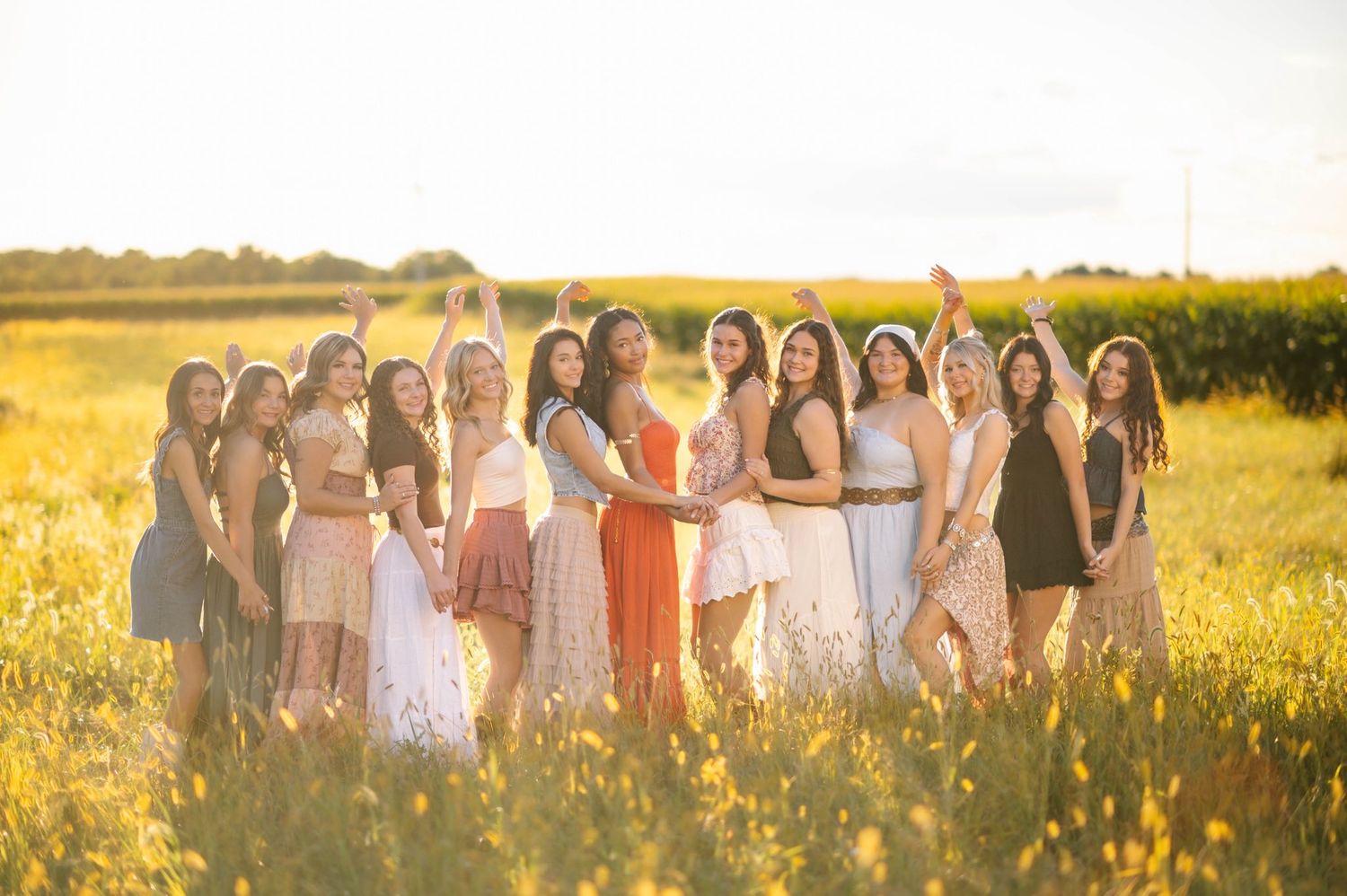 A line of people in dresses stand together in a golden meadow at sunset.