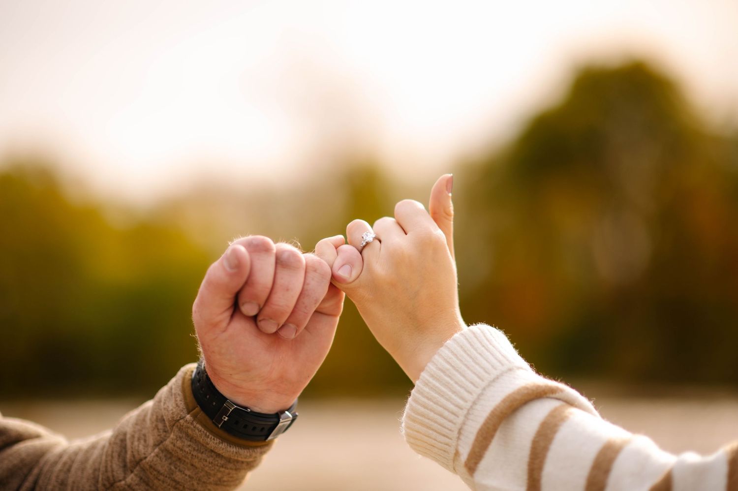 Close-up of hands reaching toward each other against blurred autumn background.