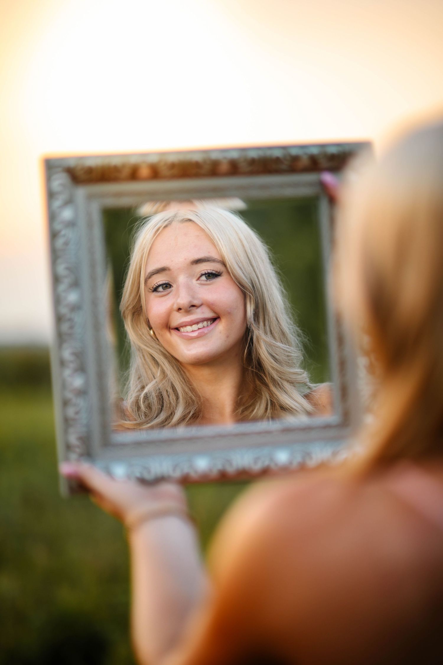 Reflections appear in a vintage silver frame held up against a warm sunset backdrop.