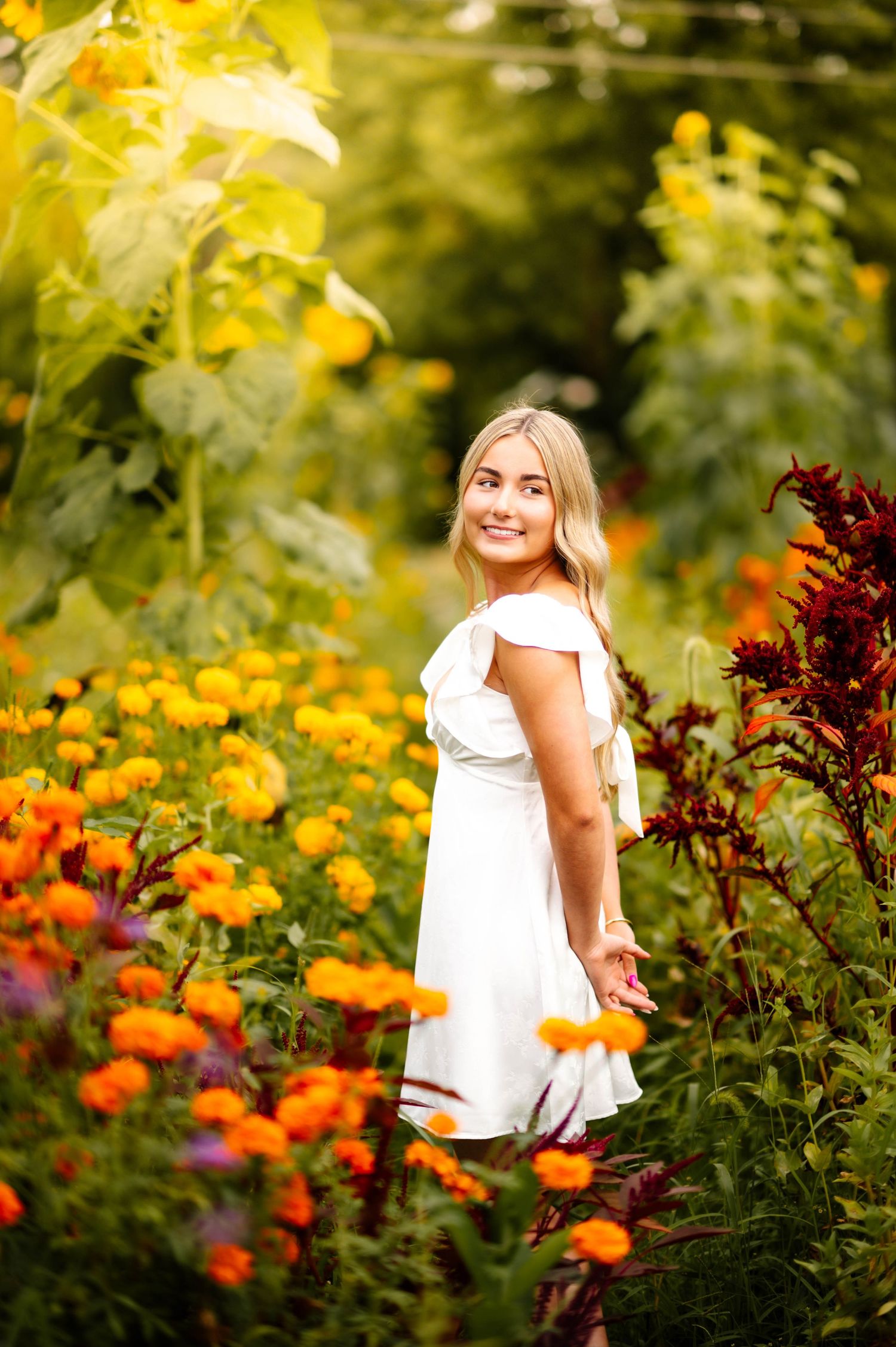 A dreamy summer photoshoot in a garden with vibrant yellow and orange flowers creating a beautiful natural backdrop.