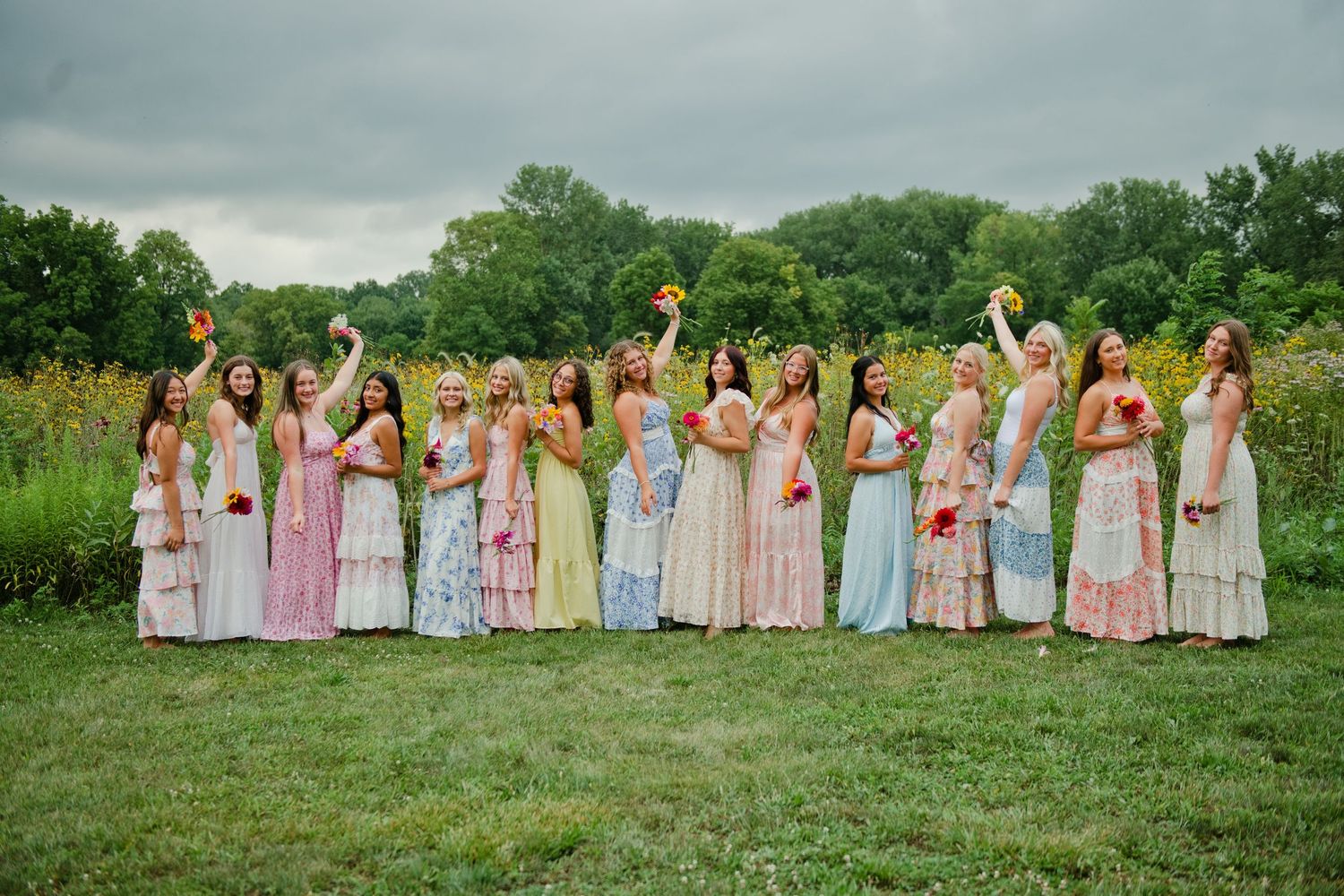 Bridesmaids in colorful pastel gowns celebrating outdoors, raising bouquets in a lush garden setting.