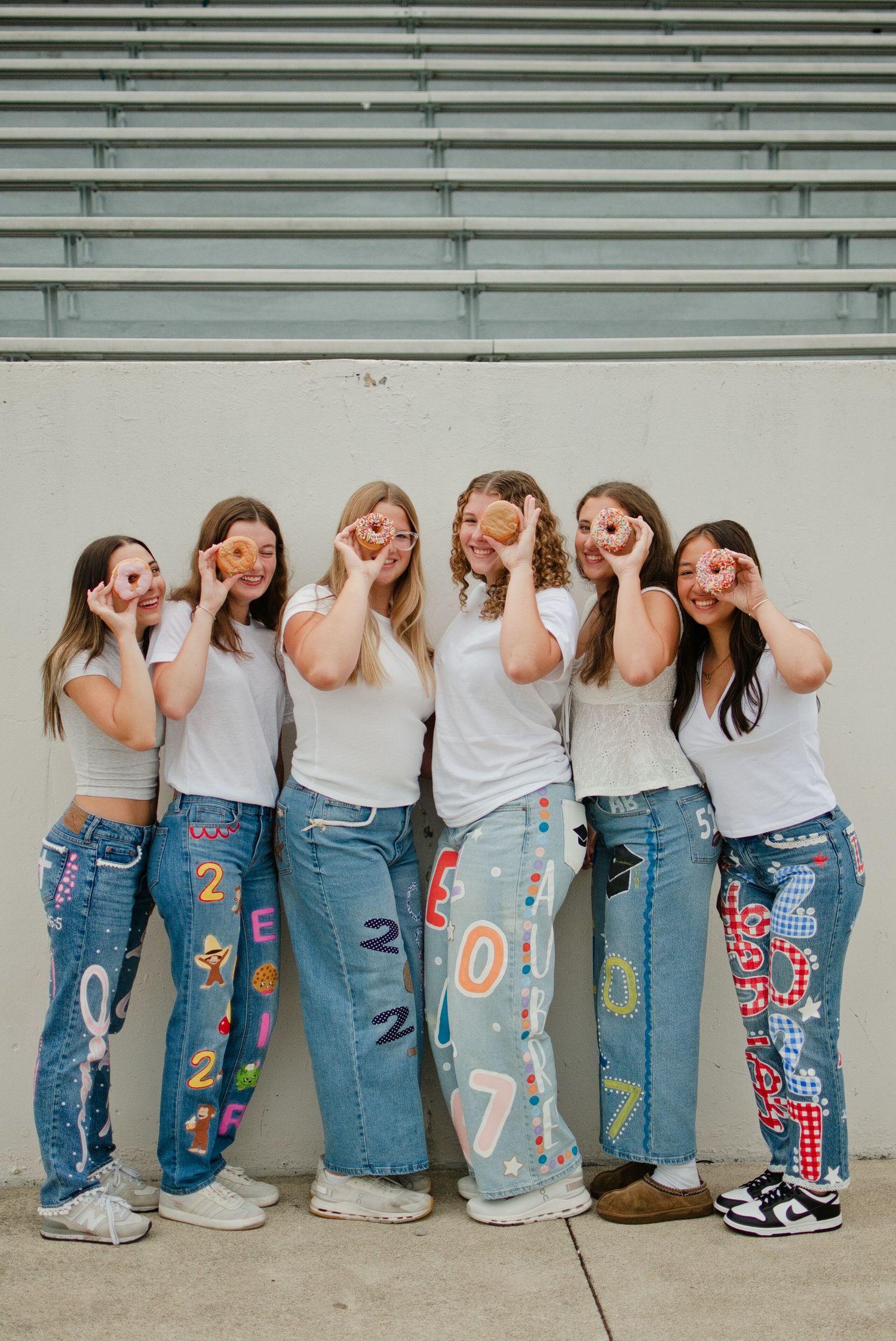 Six girls in white tees and custom painted senior 2027 jeans posing against a wall.