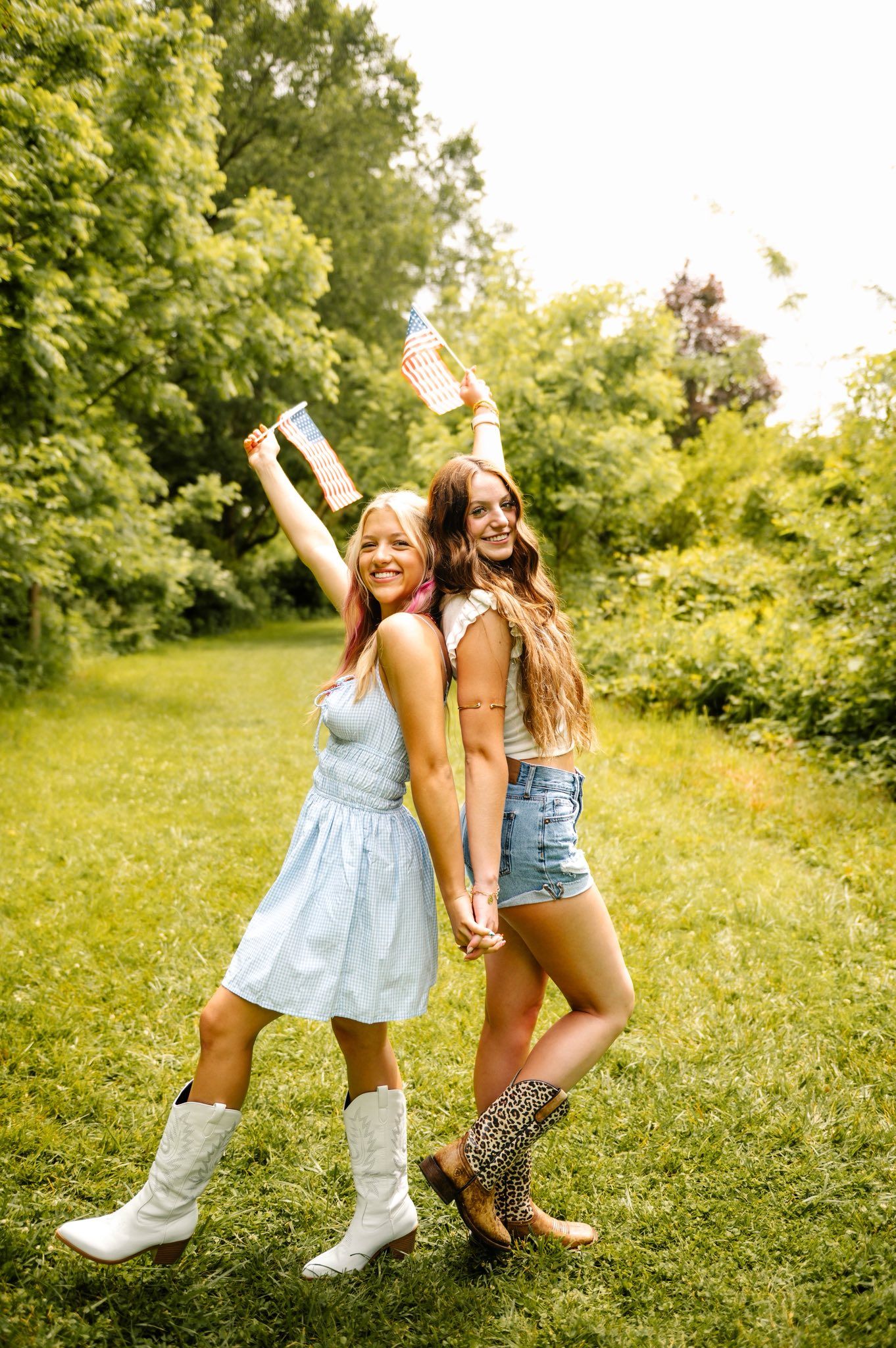 Friends in summer dresses and boots pose playfully in a sunny field.