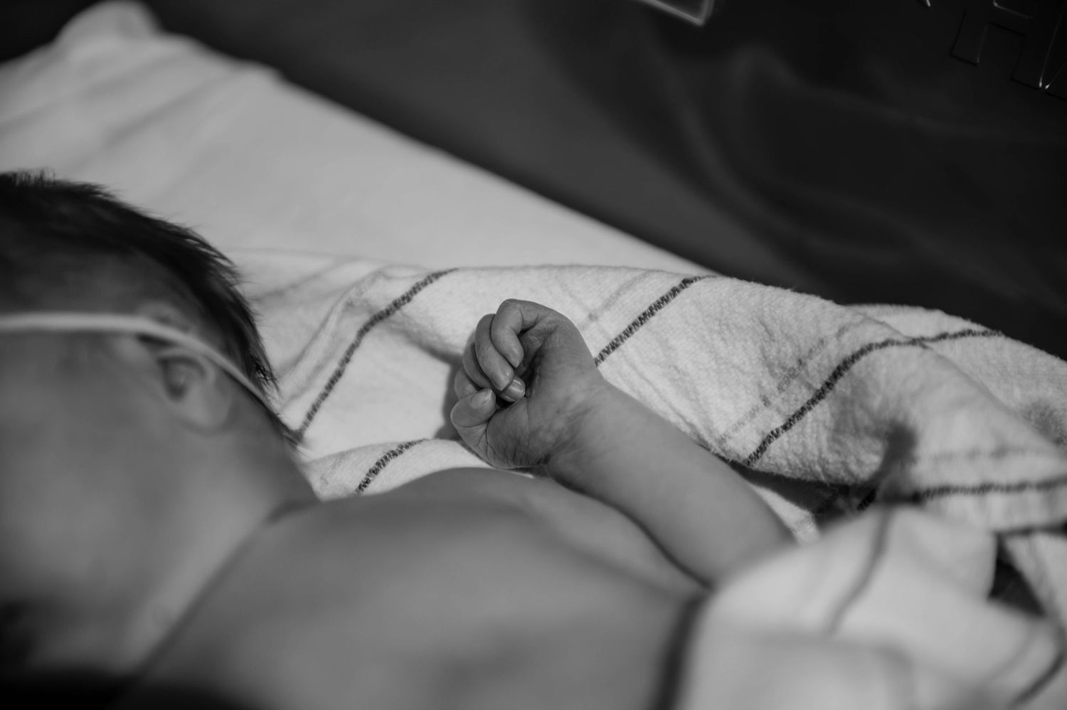 A tiny infant rests in a medical bassinet with monitoring equipment attached.