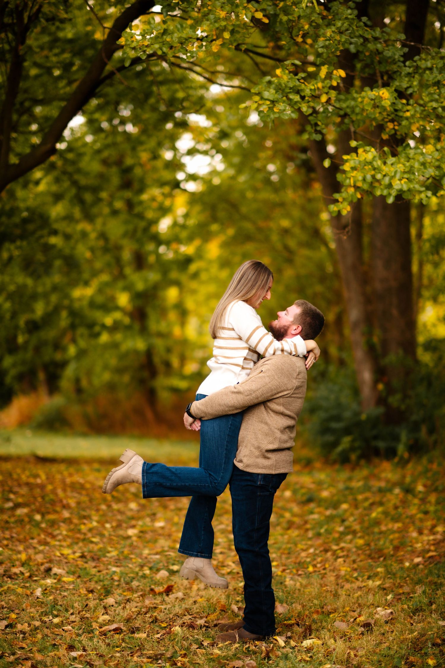 A couple shares intimate moments in a park filled with autumn leaves and golden light.