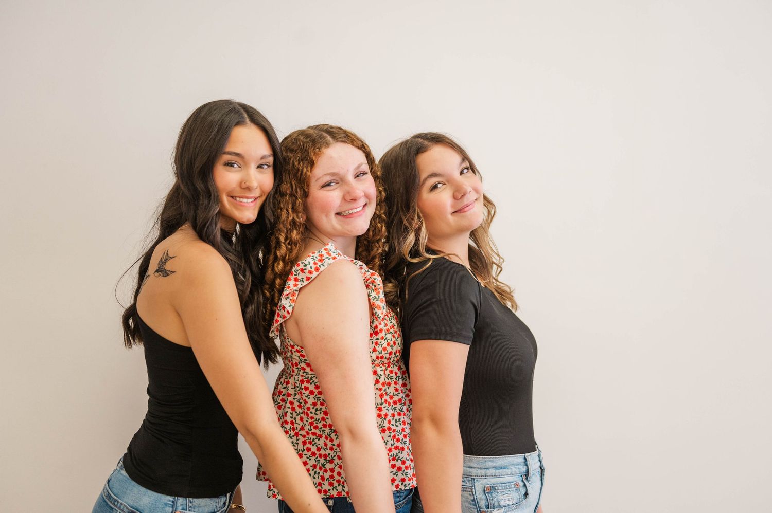 Three young women smiling and posing together against a white background in casual outfits.