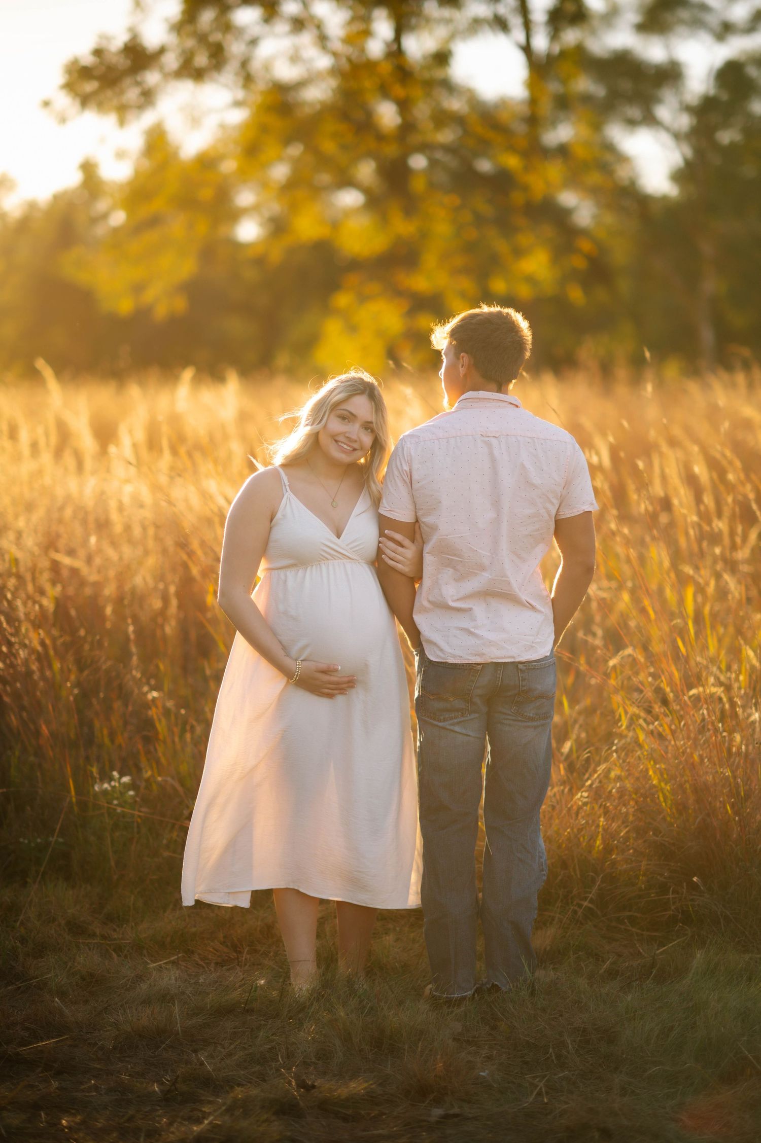 A couple shares an intimate moment in a sunlit field during golden hour.