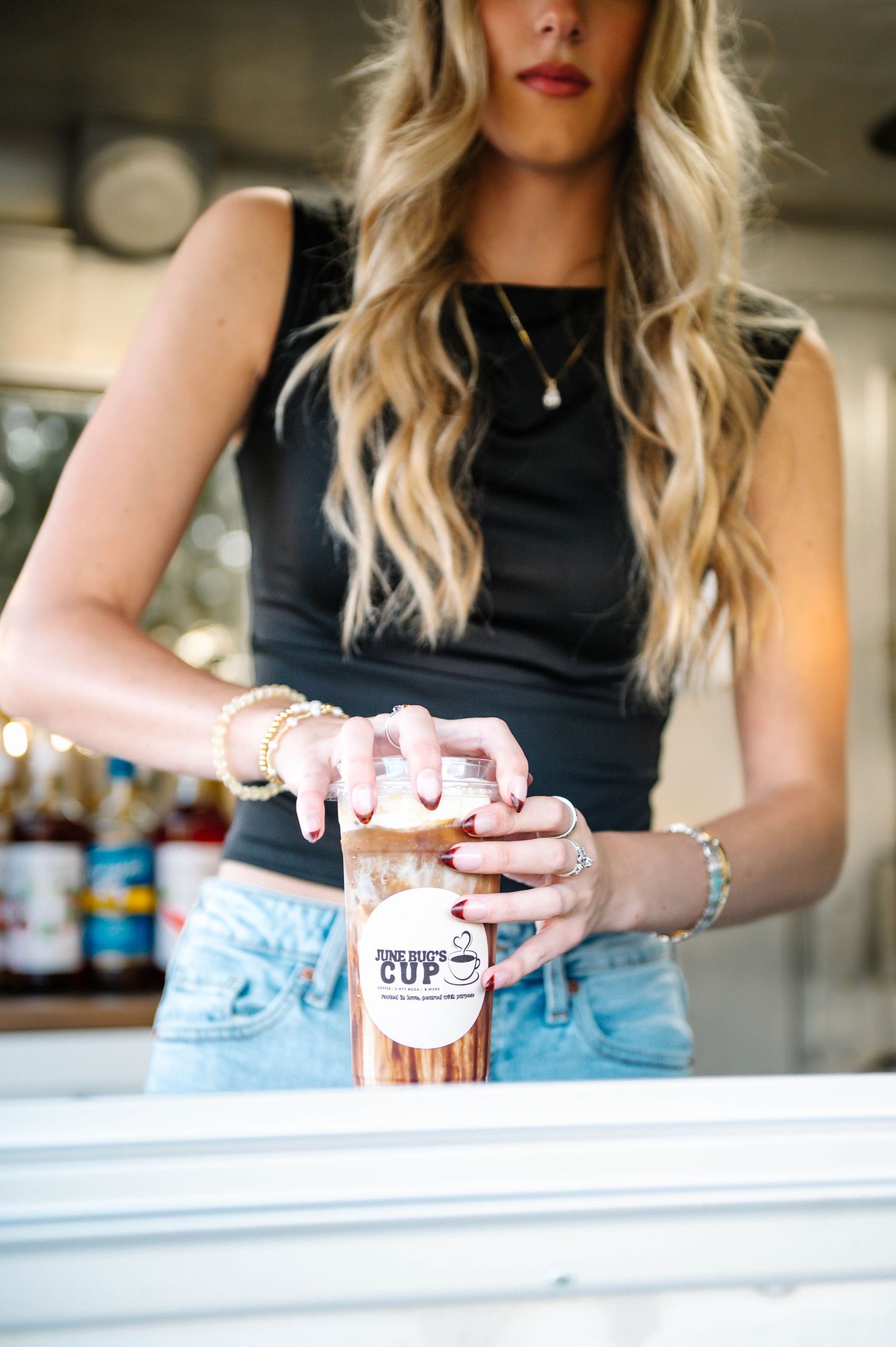 Woman in black tank top and light jeans serving drinks from a coffee food truck window.