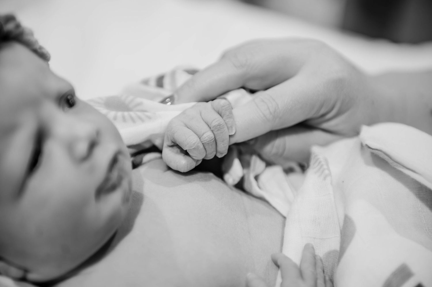 Black and white image showing hands tenderly caring for a swaddled infant.