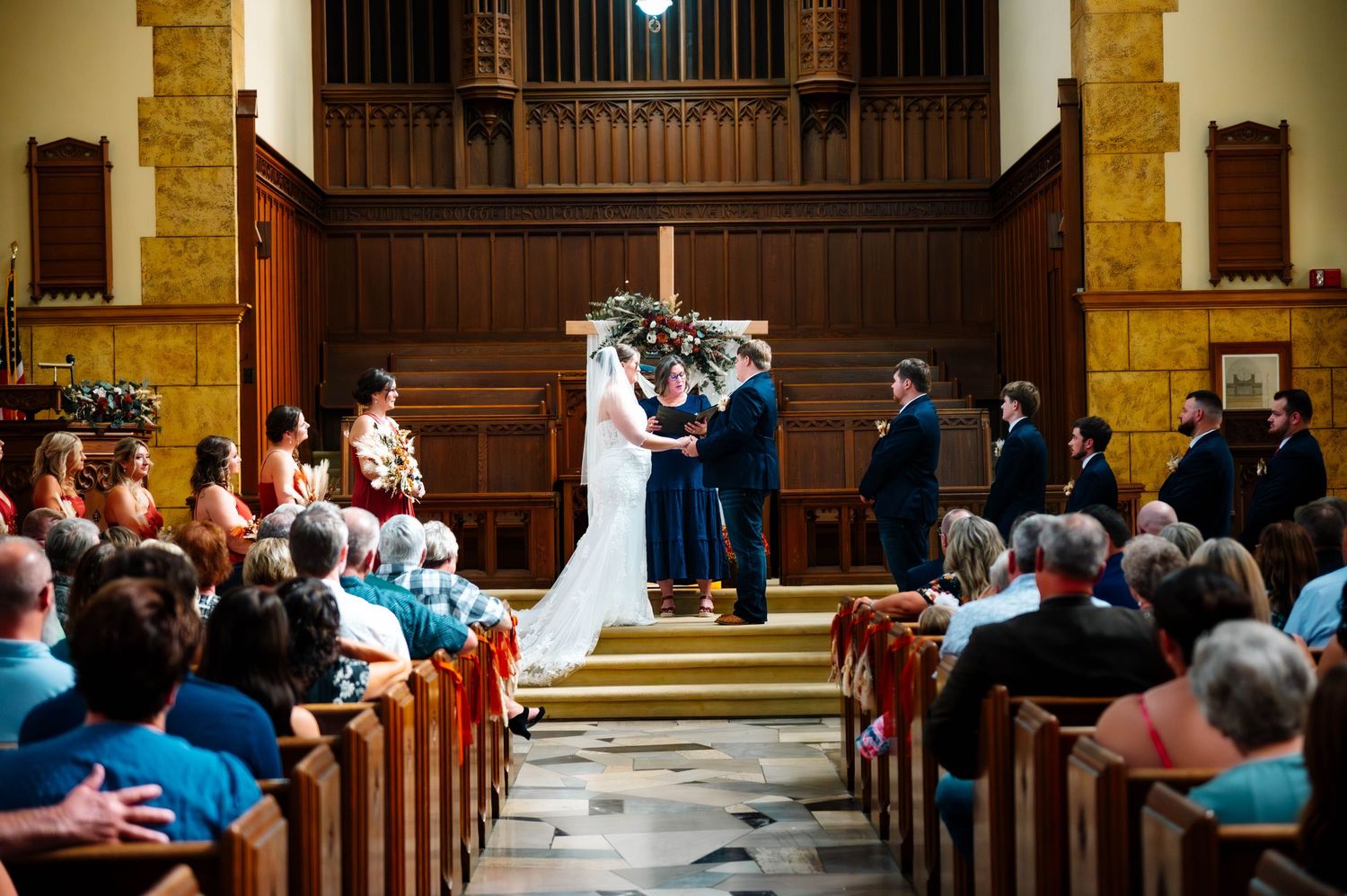 Wide angle view of a church wedding ceremony with guests seated in wooden pews.