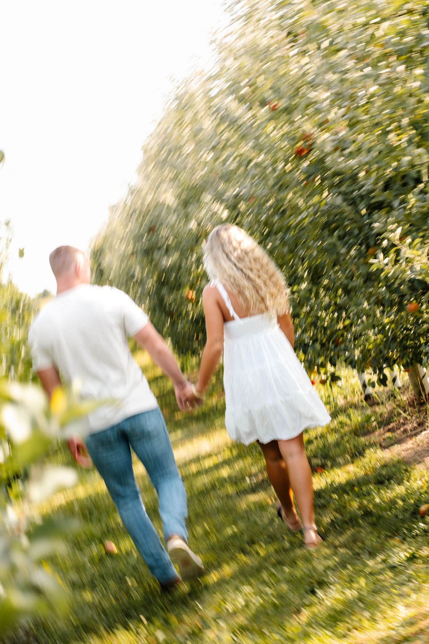 Couple running hand in hand through a sun-dappled garden path in casual summer attire.