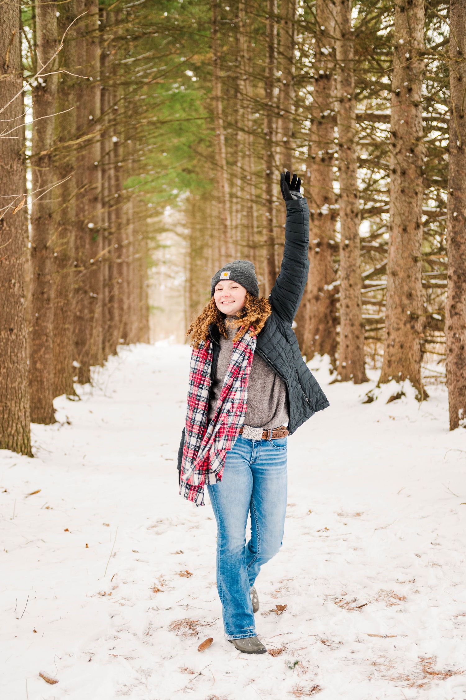 Person in plaid shirt and jeans playing in snowy winter forest path.
