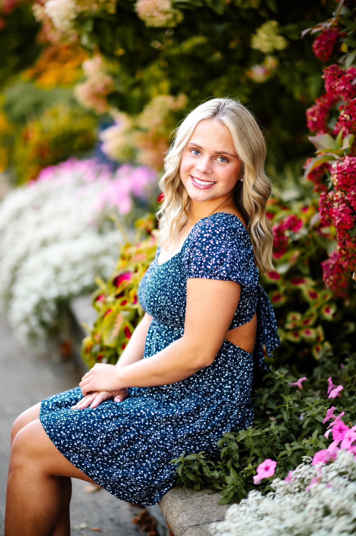 A series of outdoor portrait photos showing someone in a blue polka dot dress posing among colorful garden flowers.
