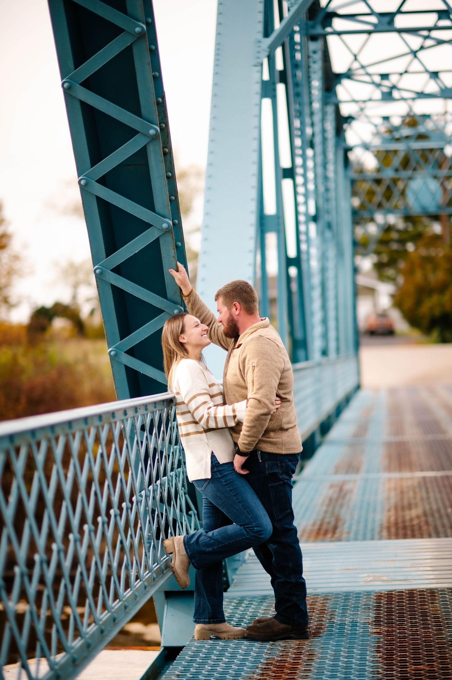 Couple shares intimate moment on vintage steel bridge during sunset.