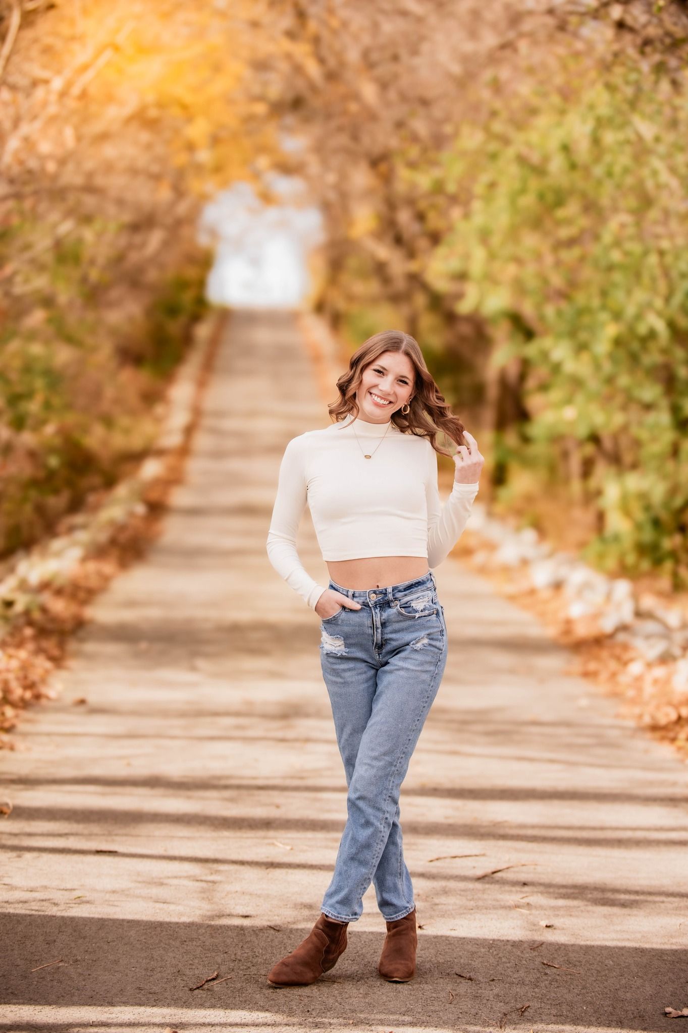 Portrait of someone in casual attire on an autumn path surrounded by golden foliage.