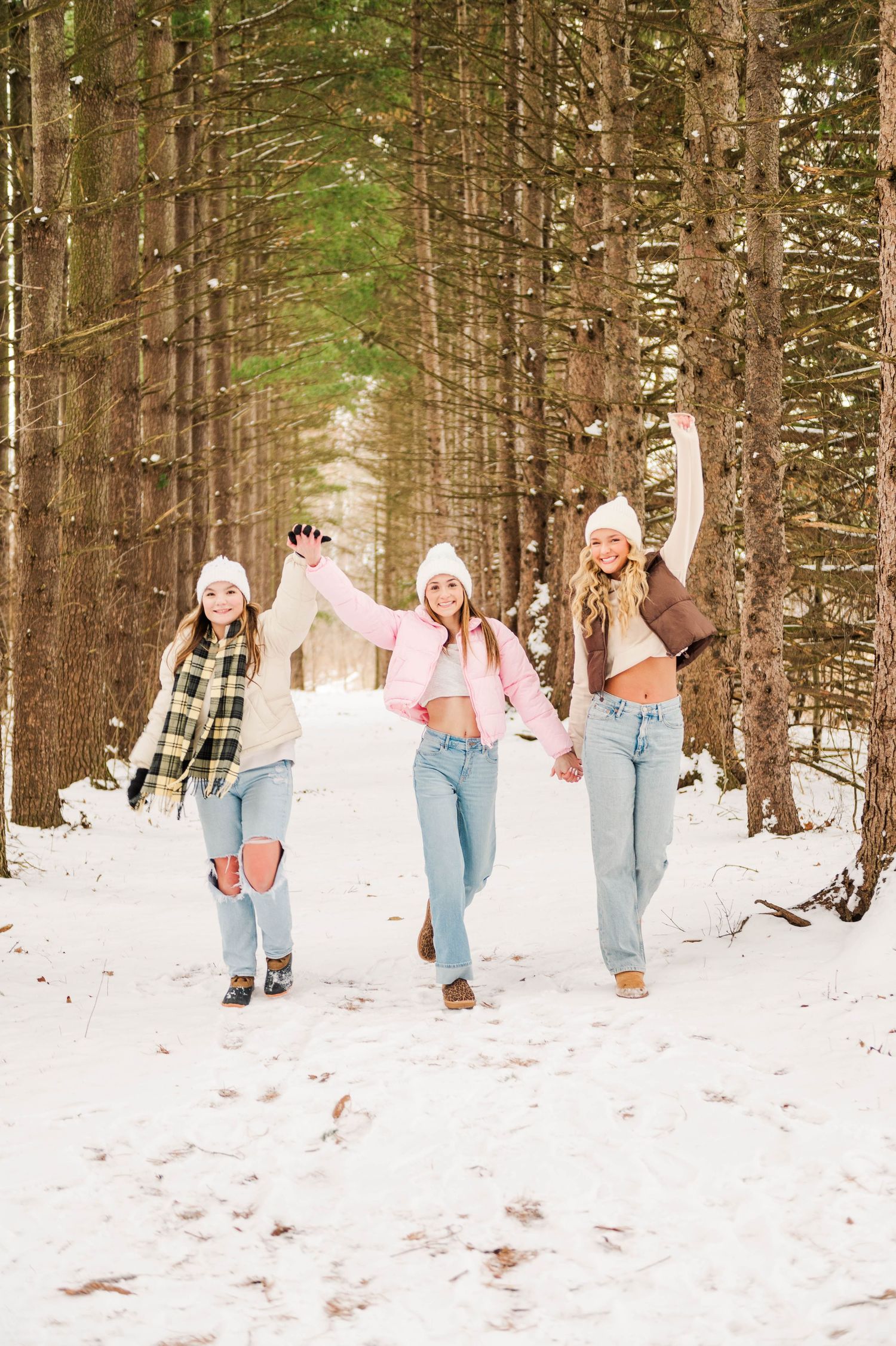 Friends hold hands and jump joyfully on a snow-covered forest path.