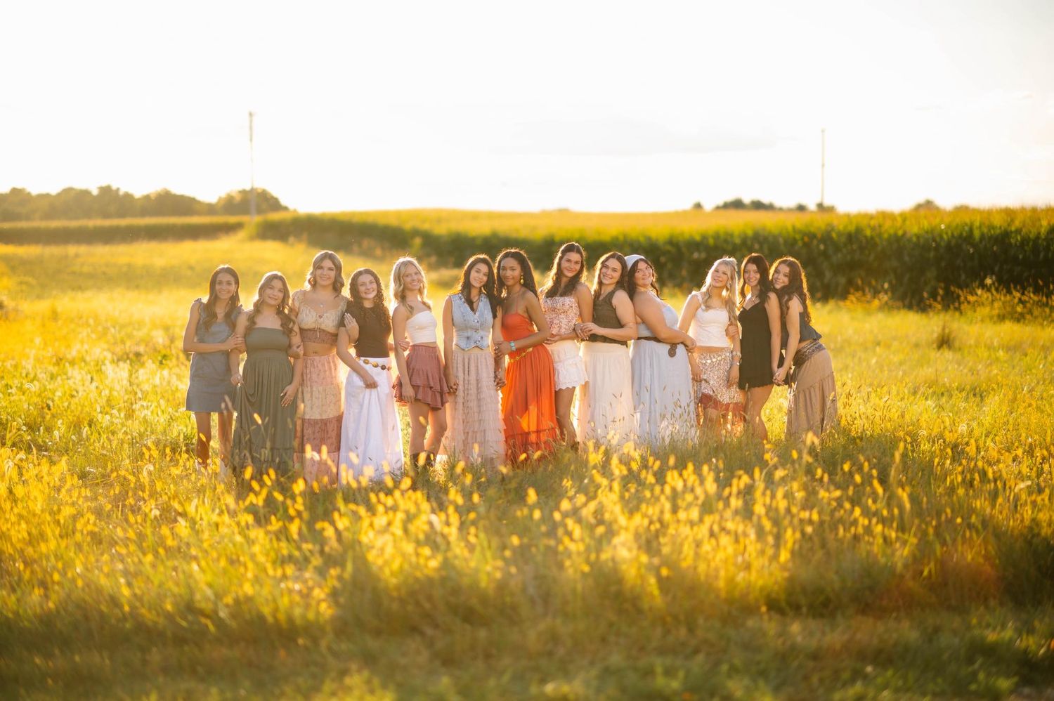 Large group portrait in flowing dresses standing among wildflowers at sunset.